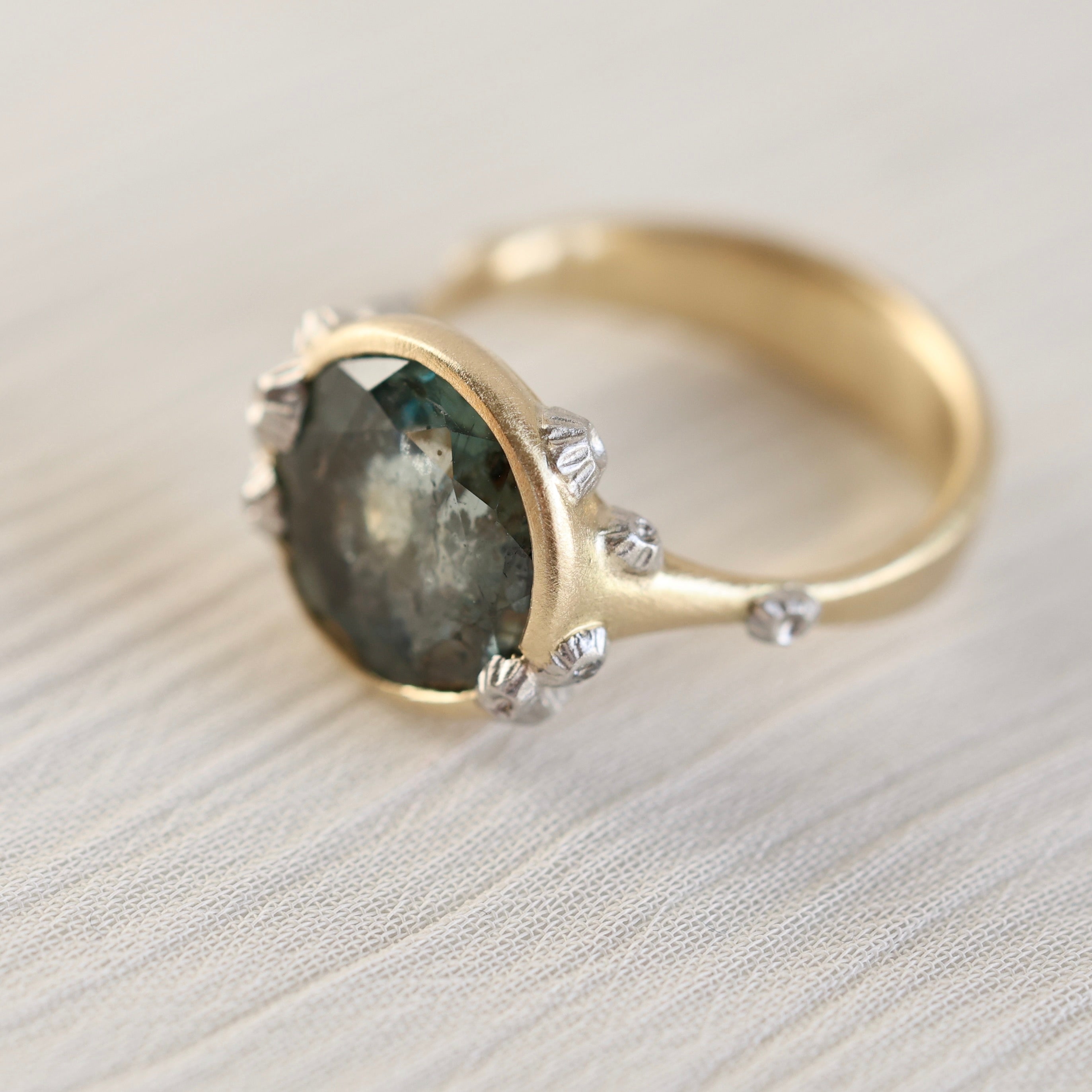 Gold ring with a green gemstone and barnacles on a light background