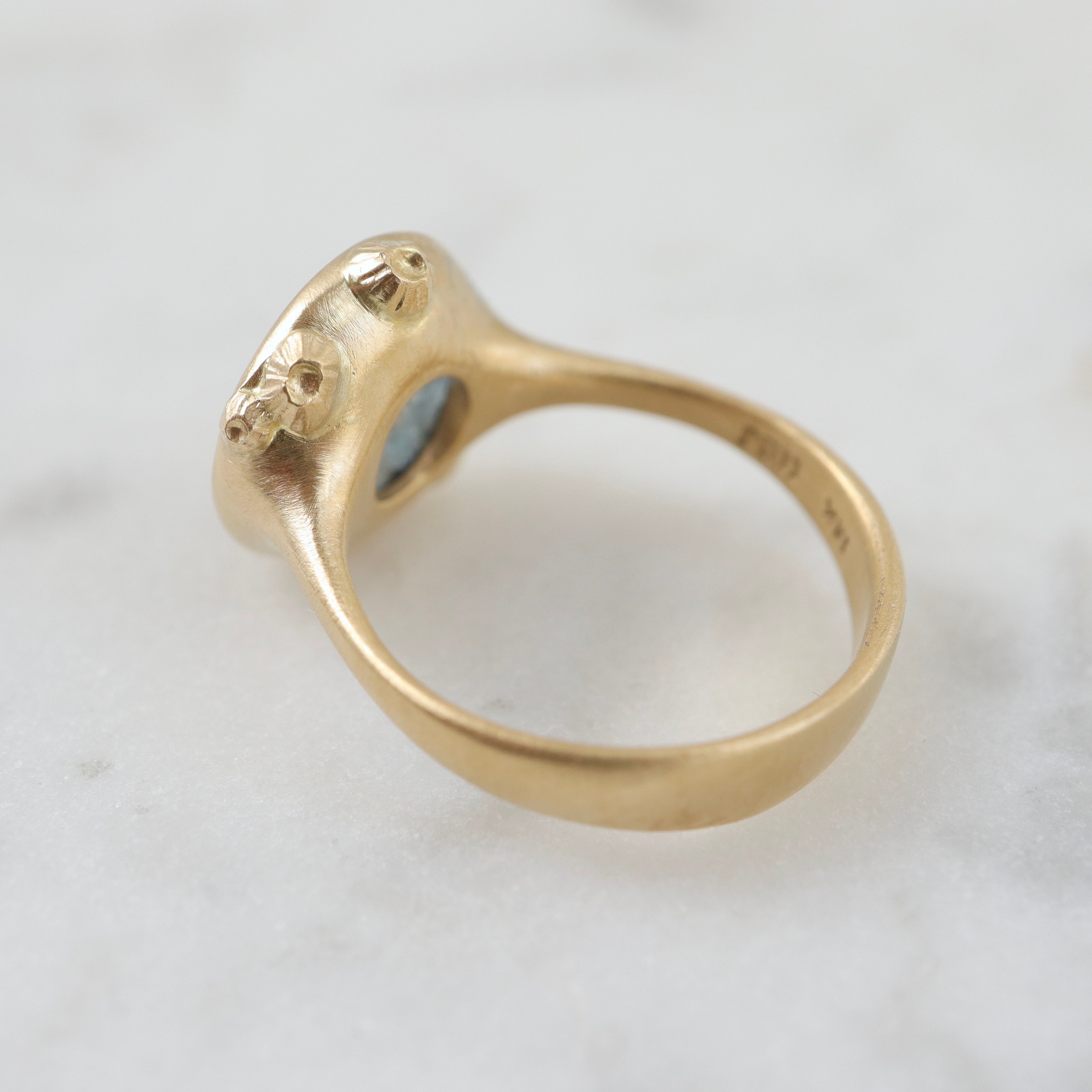 steely blue color change sapphire set in a gold bezel and band. Around the cup of the bezel are tiny gold barnacles. Photographed back view and in natural light.