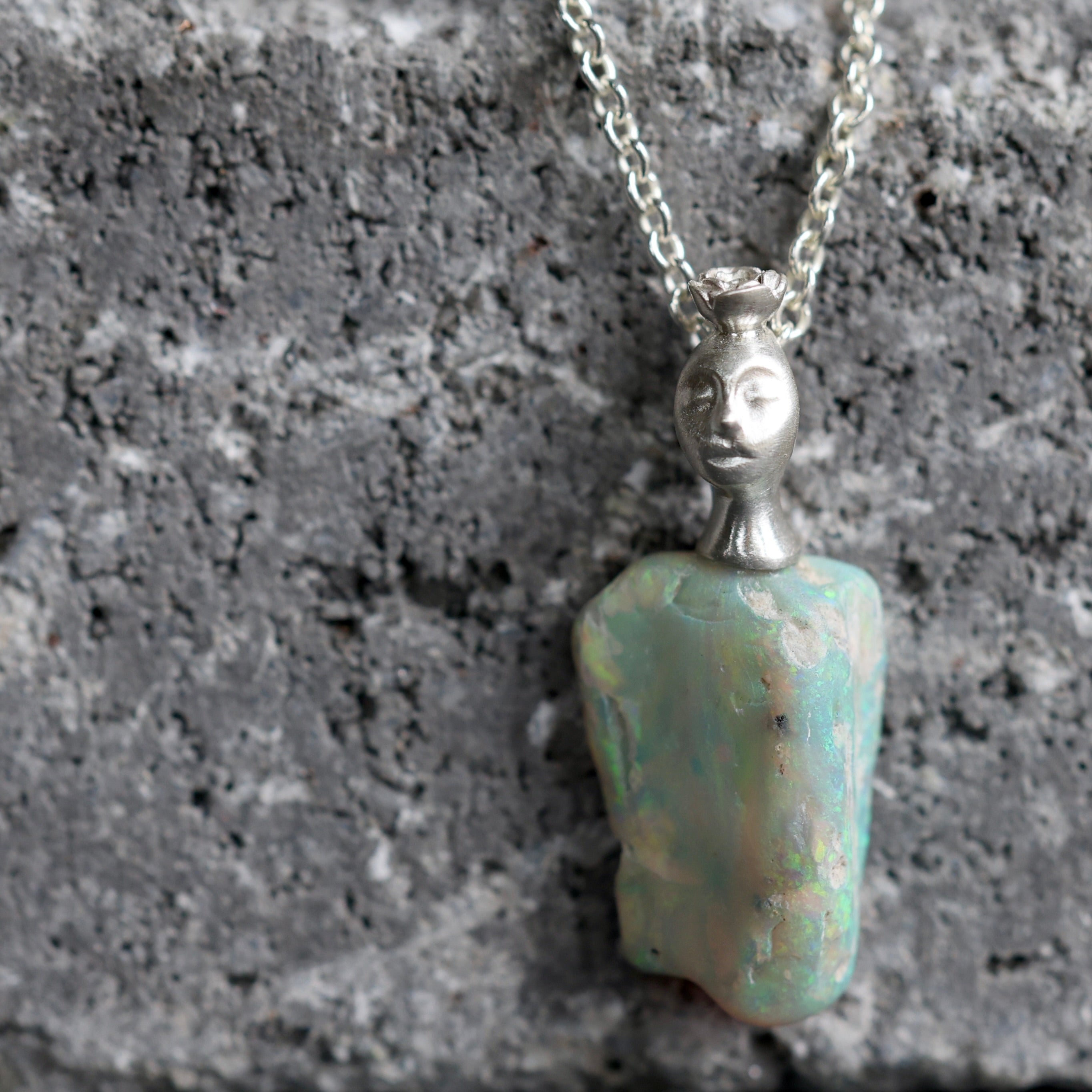 Necklace with an opal pendant featuring a face on a textured gray surface