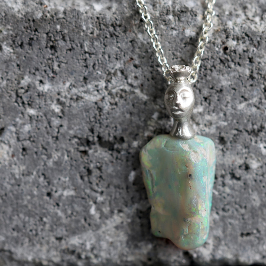 Necklace with an opal pendant featuring a face on a textured gray surface