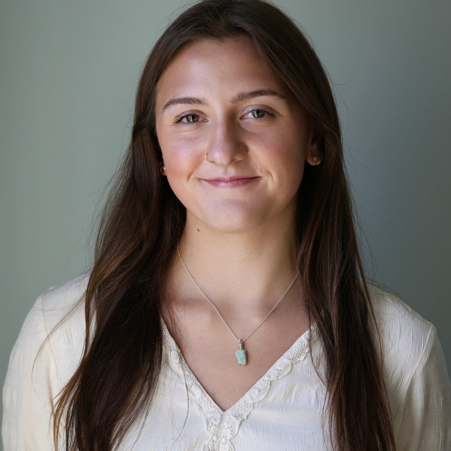 Woman with long brown hair wearing a white blouse and a necklace against a plain background