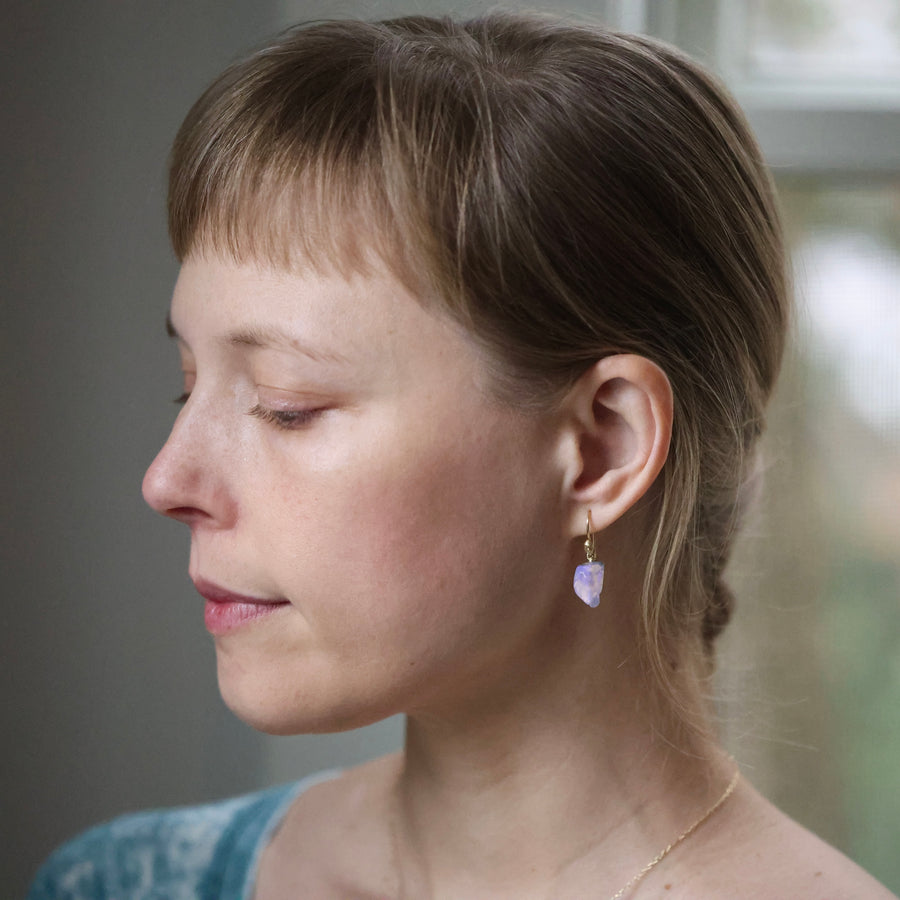 Woman with blond hair wearing earrings and a necklace, looking down.