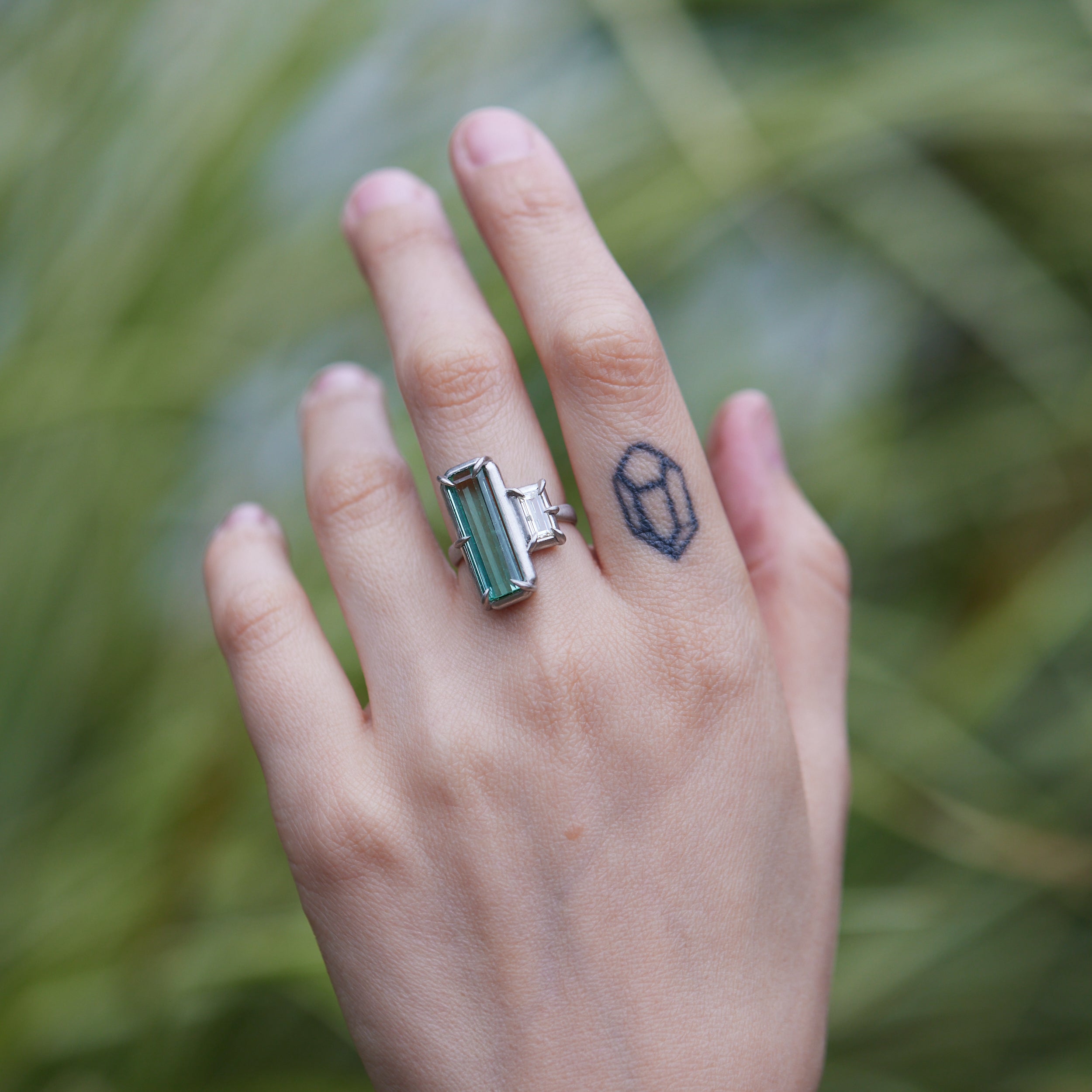 long, rectangular tourmaline stone set with prongs next to a diamond baguette. The ring is platinum, and shown on hand.