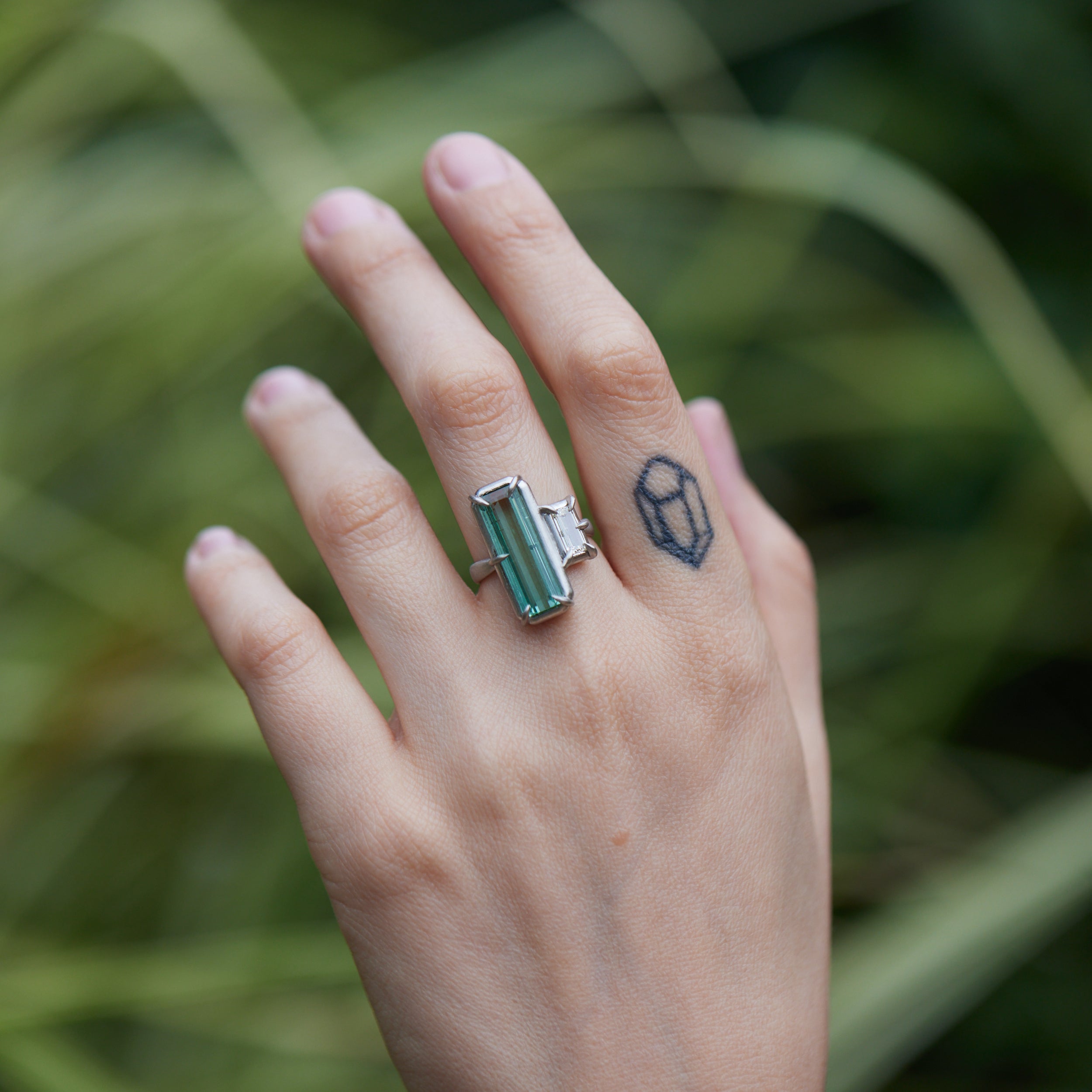 long, rectangular tourmaline stone set with prongs next to a diamond baguette. The ring is platinum, and shown on hand.