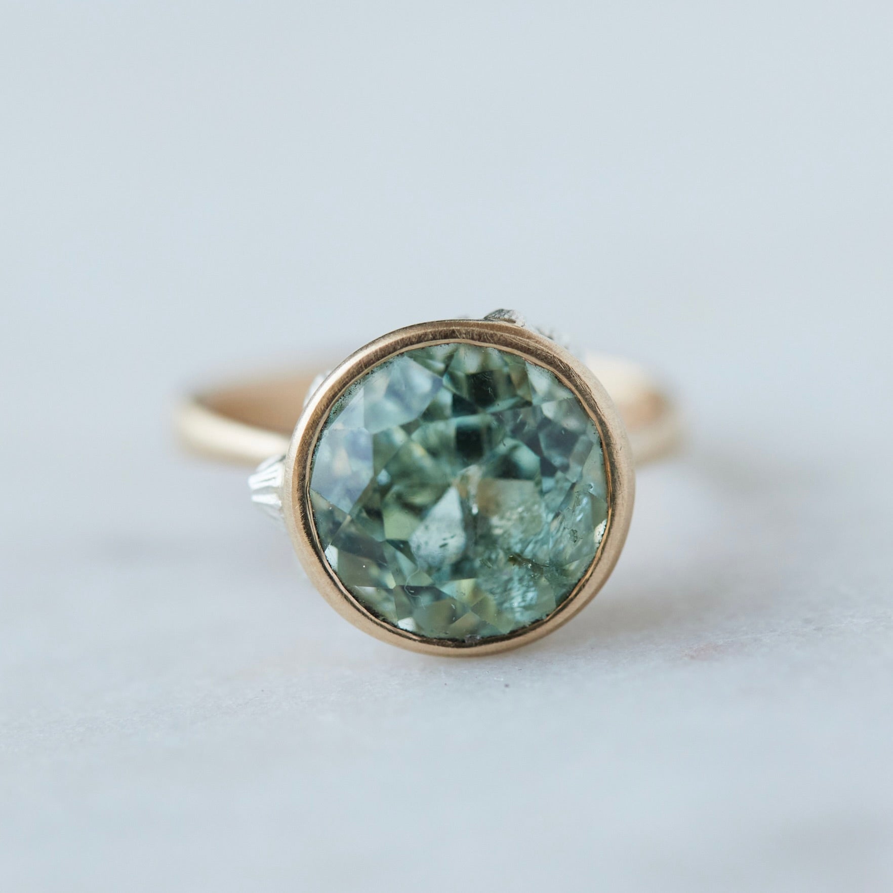 a pale mint green beryl is set in a gold bezel ring with silver barnacles. Front view.