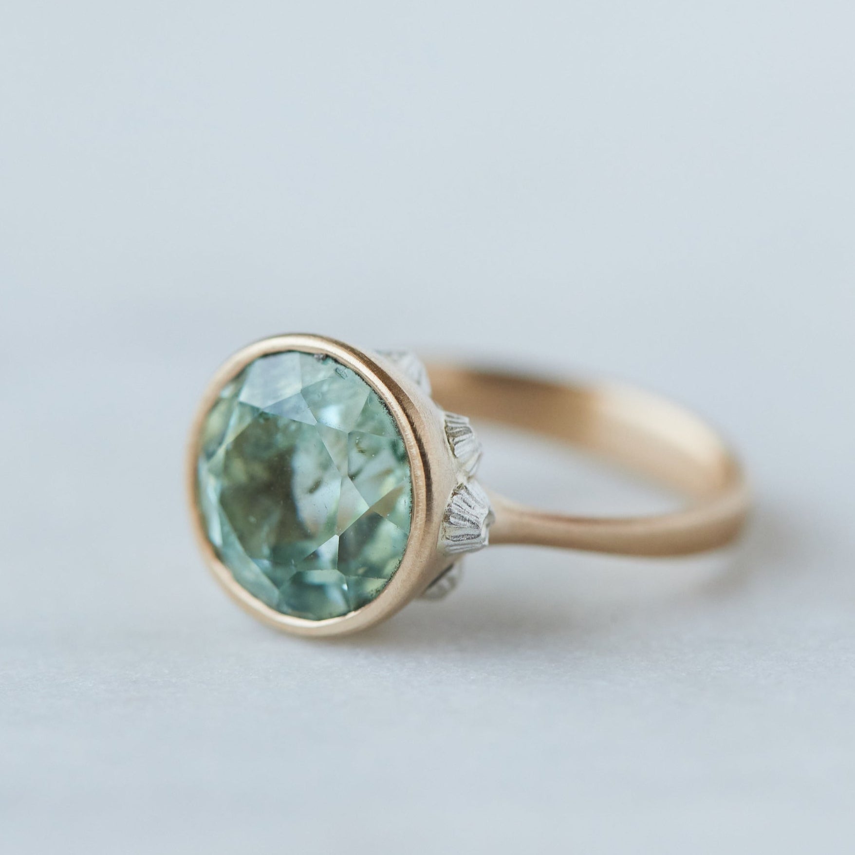 a pale mint green beryl is set in a gold bezel ring with silver barnacles. Side view.