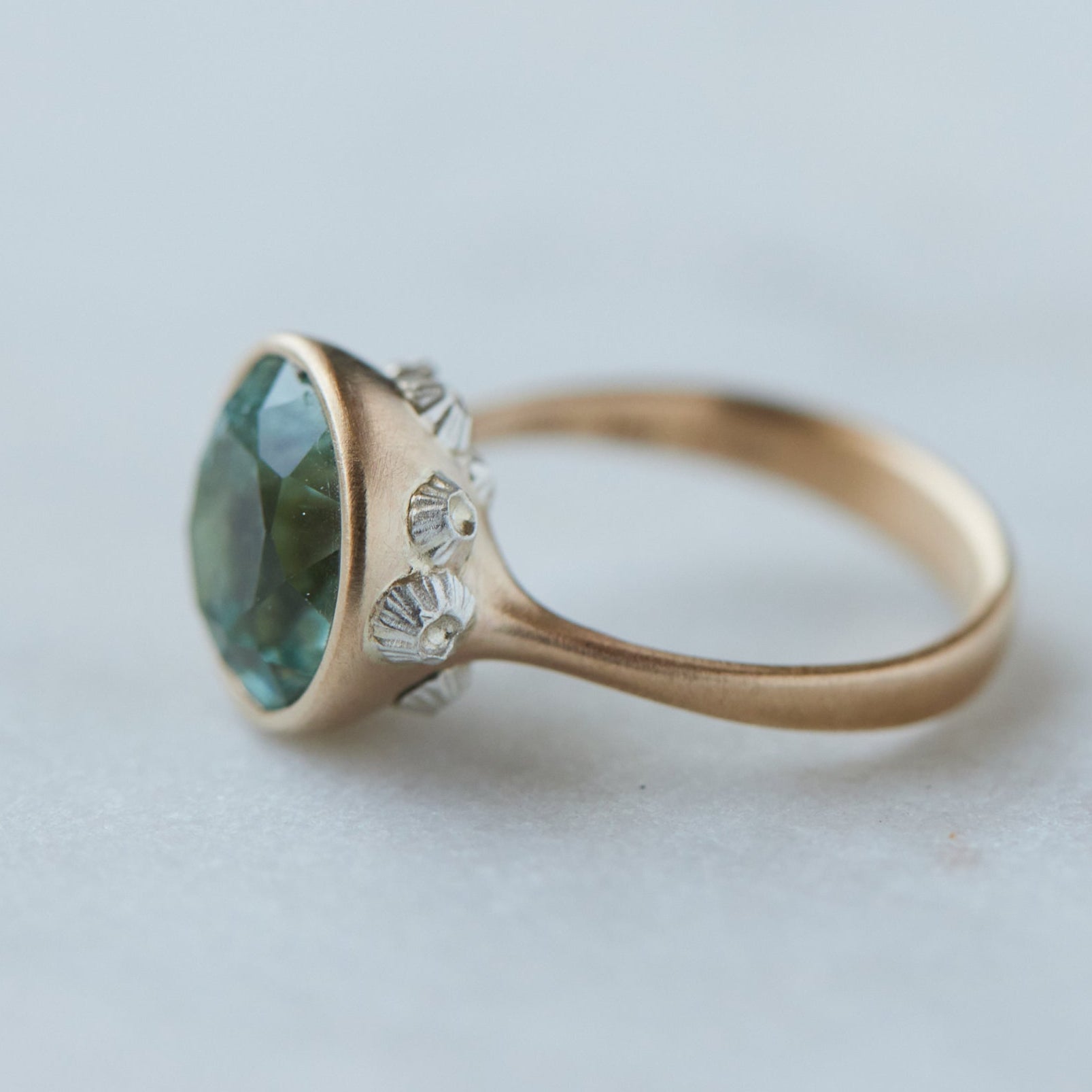 a pale mint green beryl is set in a gold bezel ring with silver barnacles. Side view.