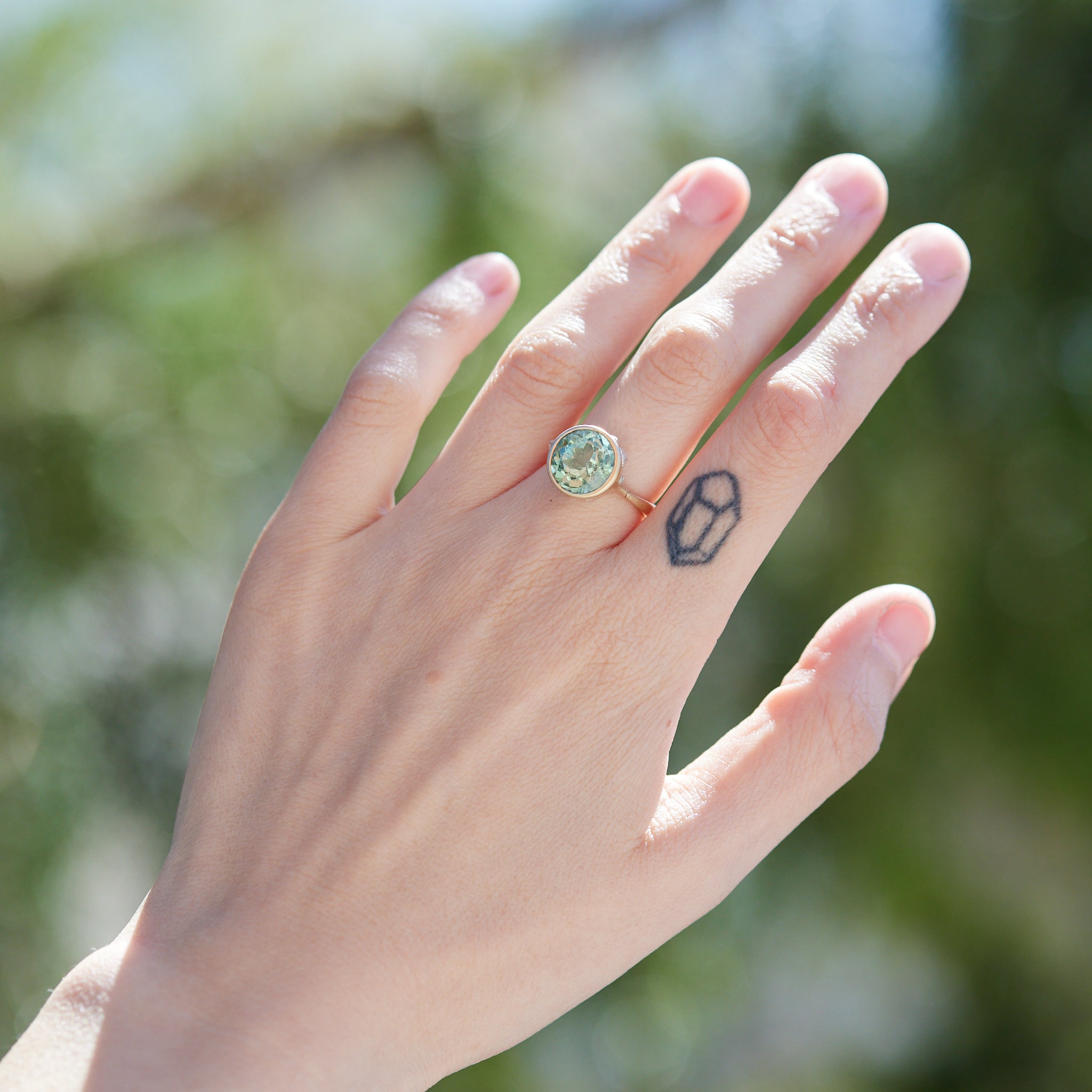 a pale mint green beryl is set in a gold bezel ring with silver barnacles. Photographed on person.