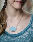 Person wearing a necklace with a blue pendant, blurred background