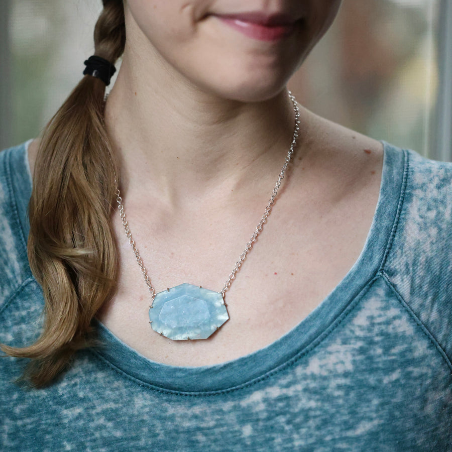 Person wearing a necklace with a blue pendant, blurred background