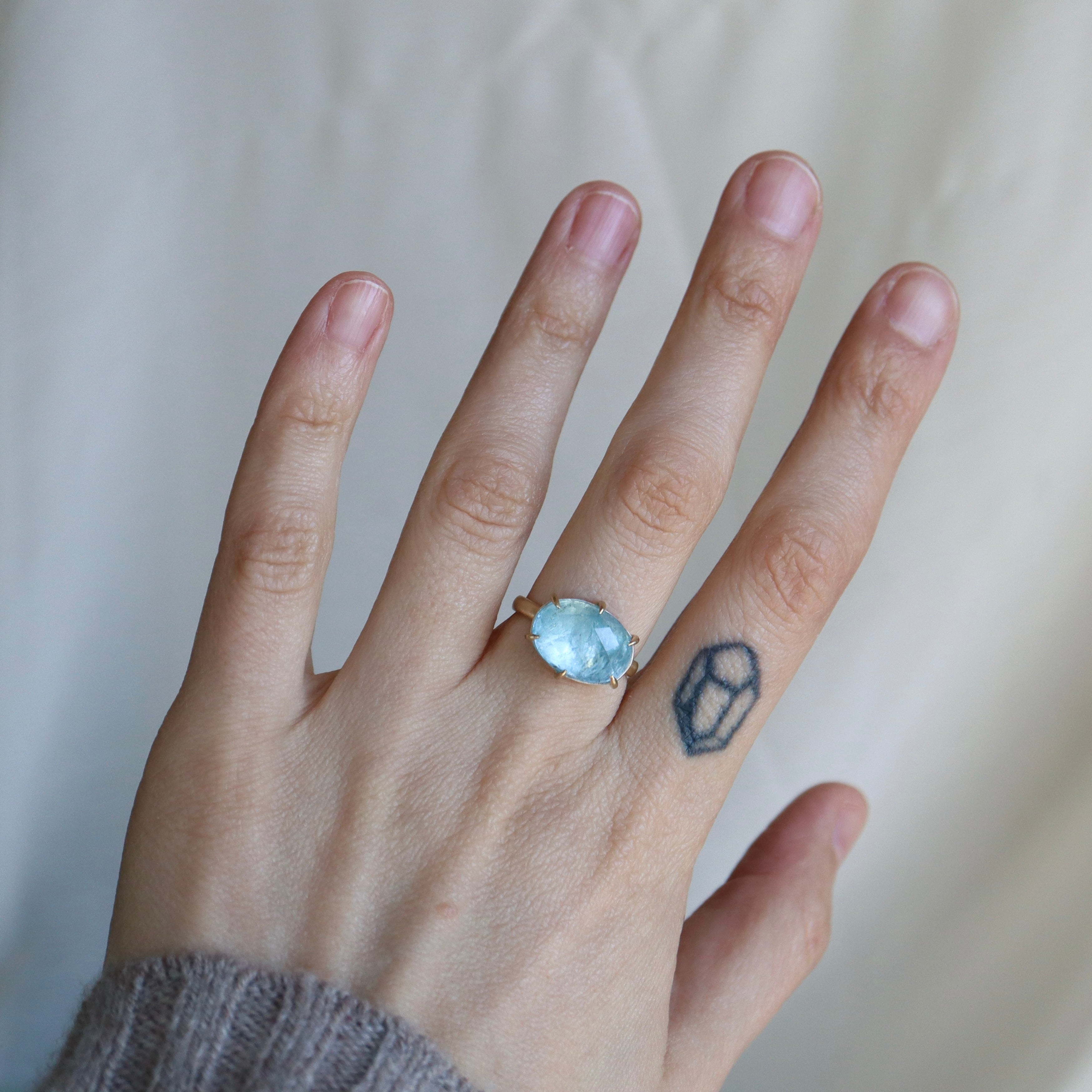 hand wearing blue gemstone ring against a pale background