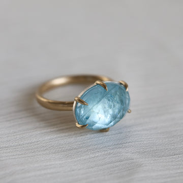 Gold ring with a blue gemstone on a light gray background