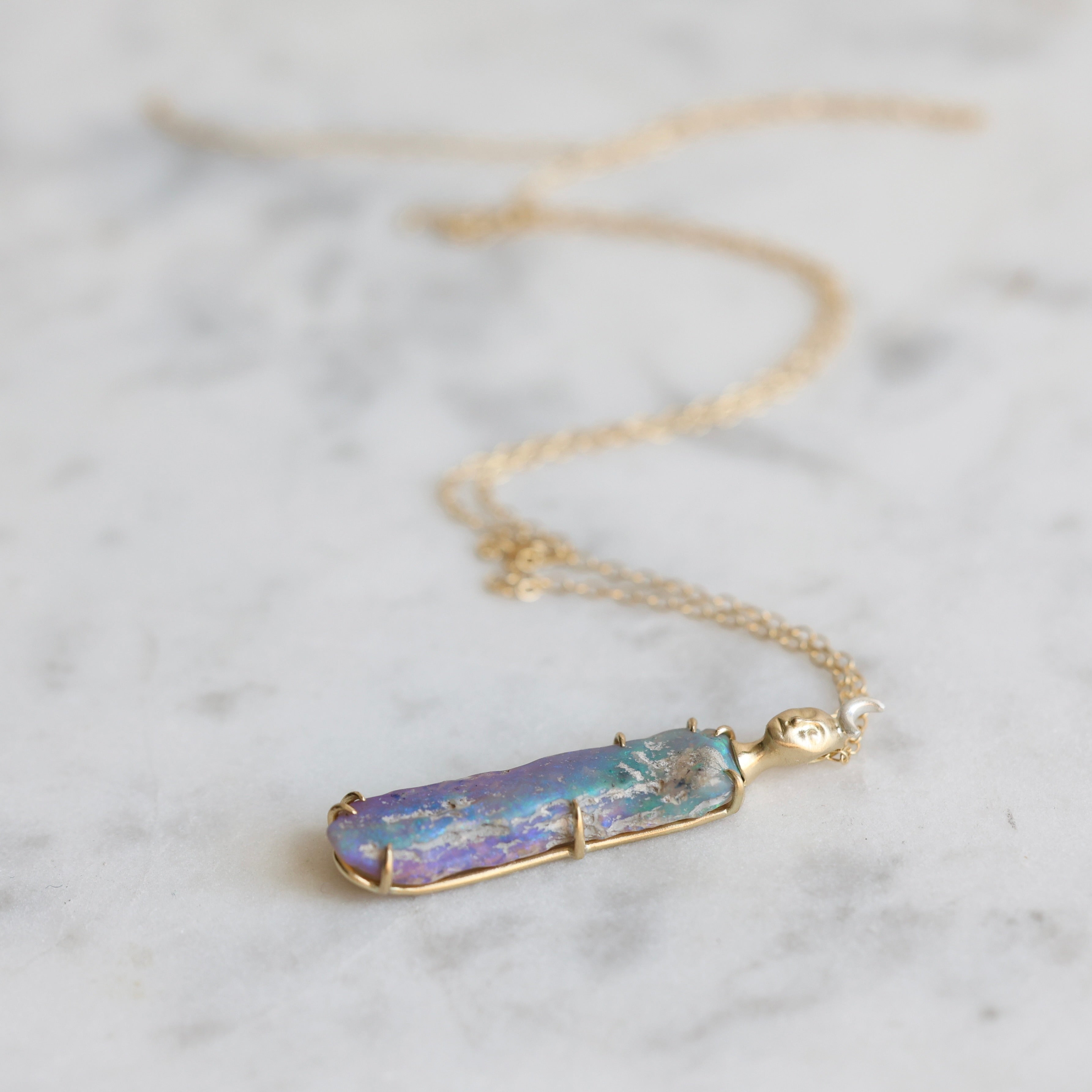 Necklace with a colorful opal and gold face with crescent moon on a marble surface