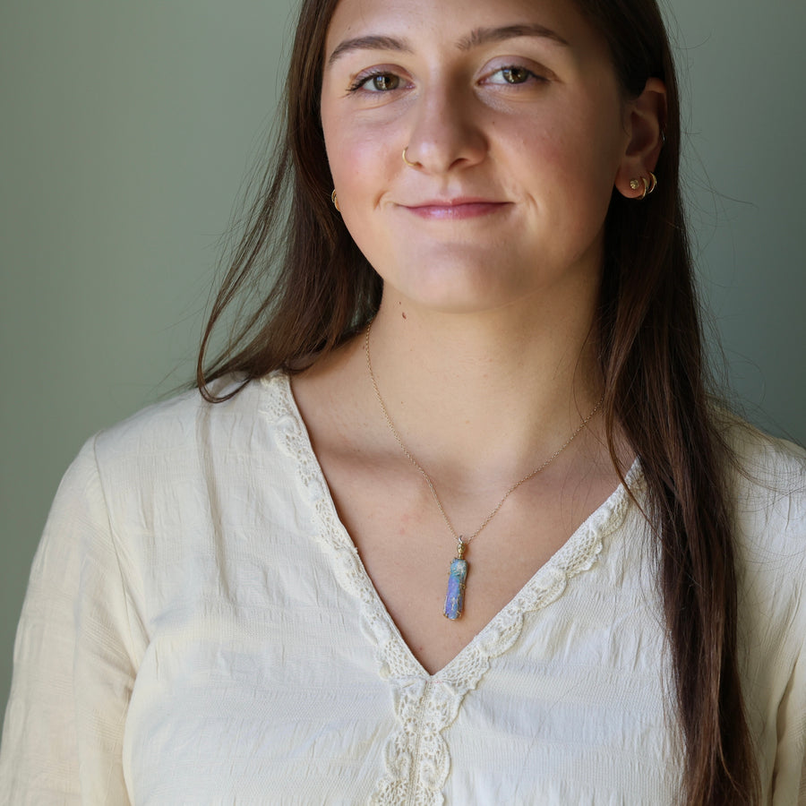 Woman wearing a white blouse and a necklace with a blue pendant against a plain background