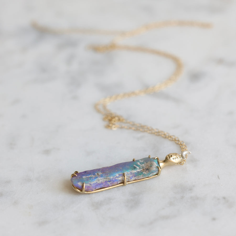 Necklace with a colorful opal and gold face with crescent moon on a marble surface