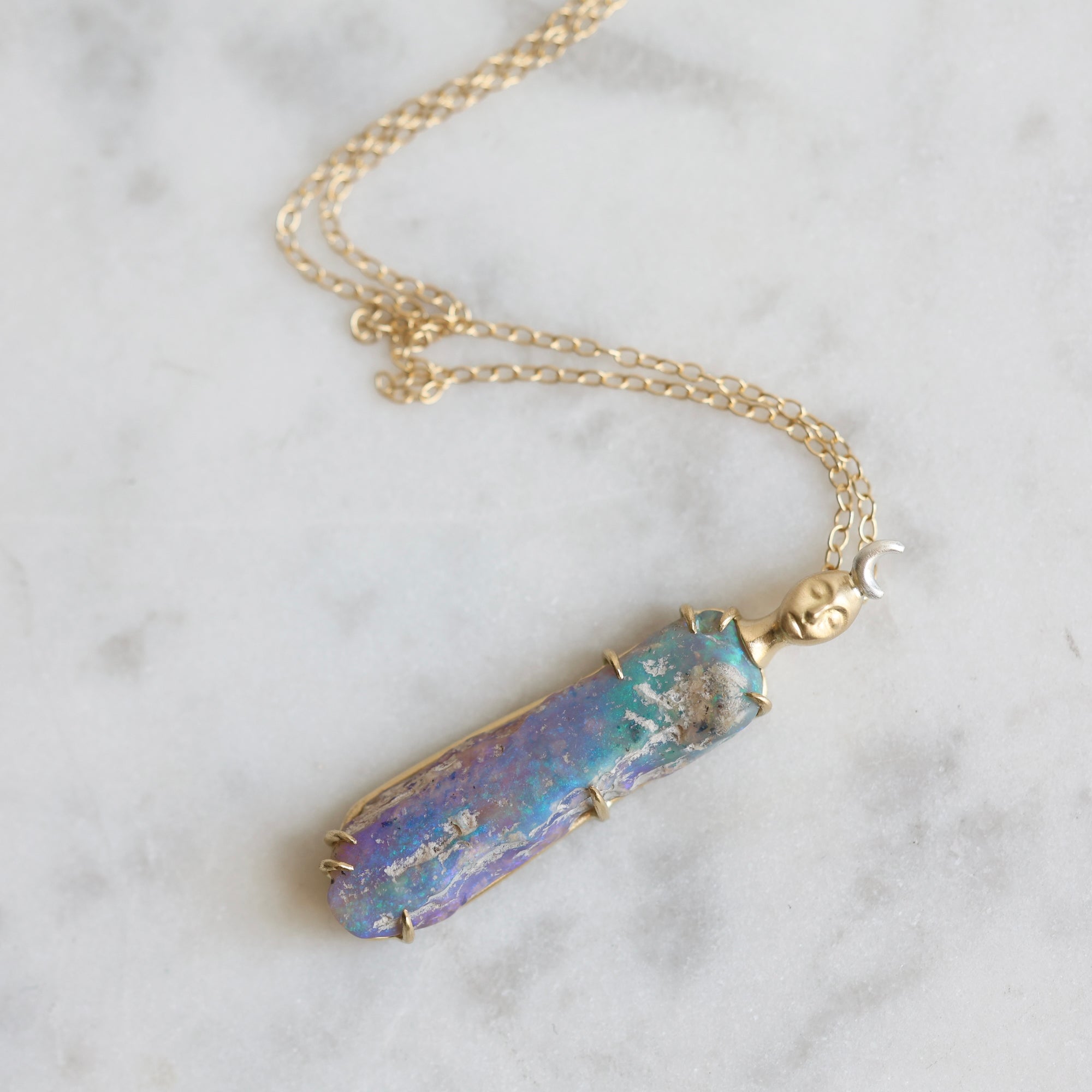 Necklace with a colorful opal and gold face with crescent moon on a marble surface