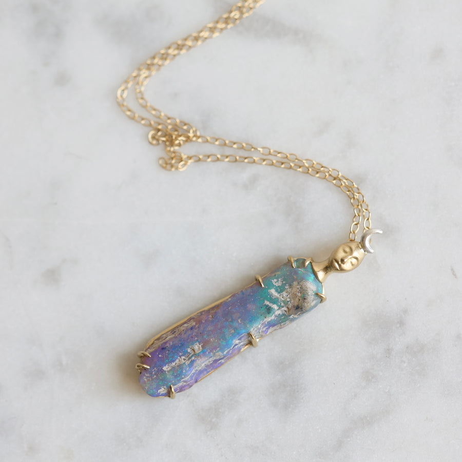 Necklace with a colorful opal and gold face with crescent moon on a marble surface