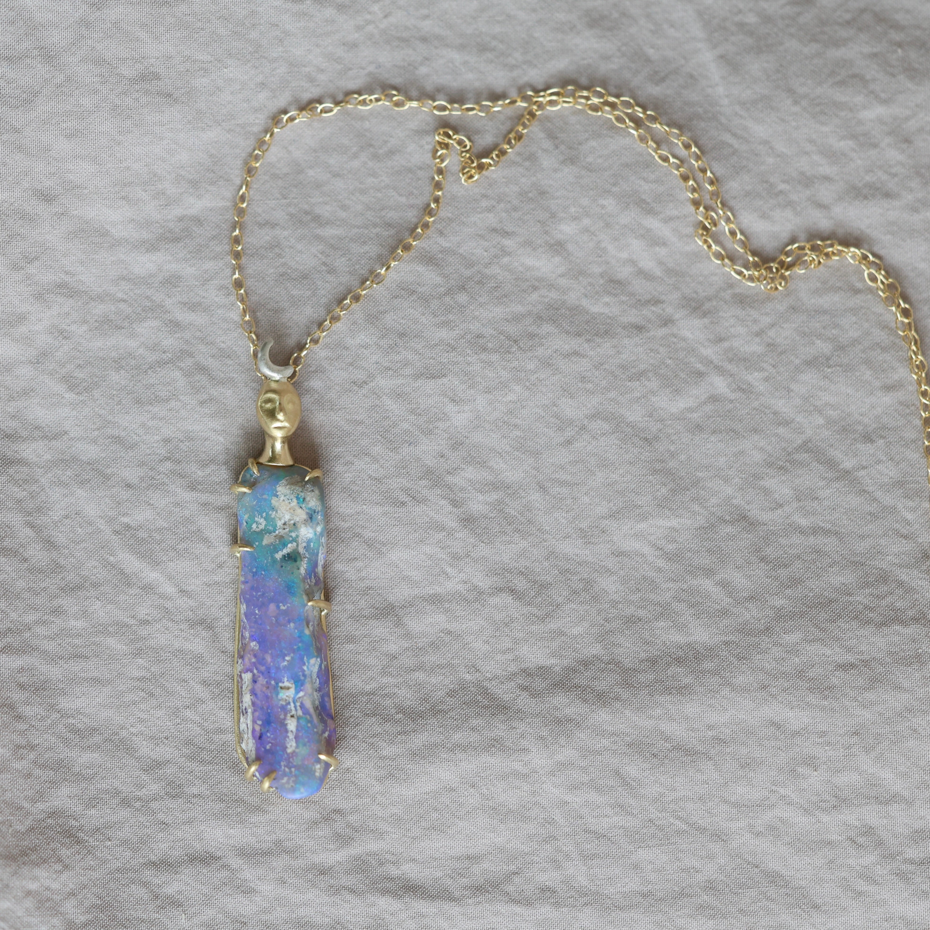 Necklace with a colorful opal and gold face with crescent moon on a textured fabric surface