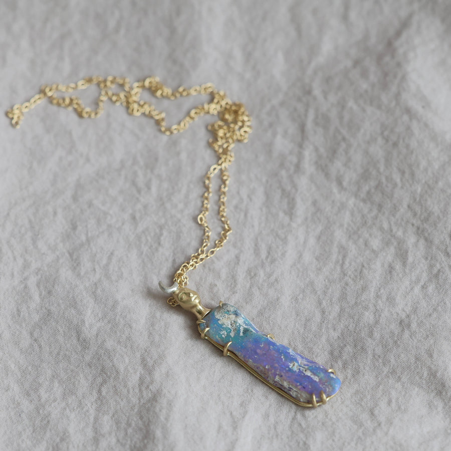 Necklace with a colorful opal and gold face with crescent moon on a textured fabric surface
