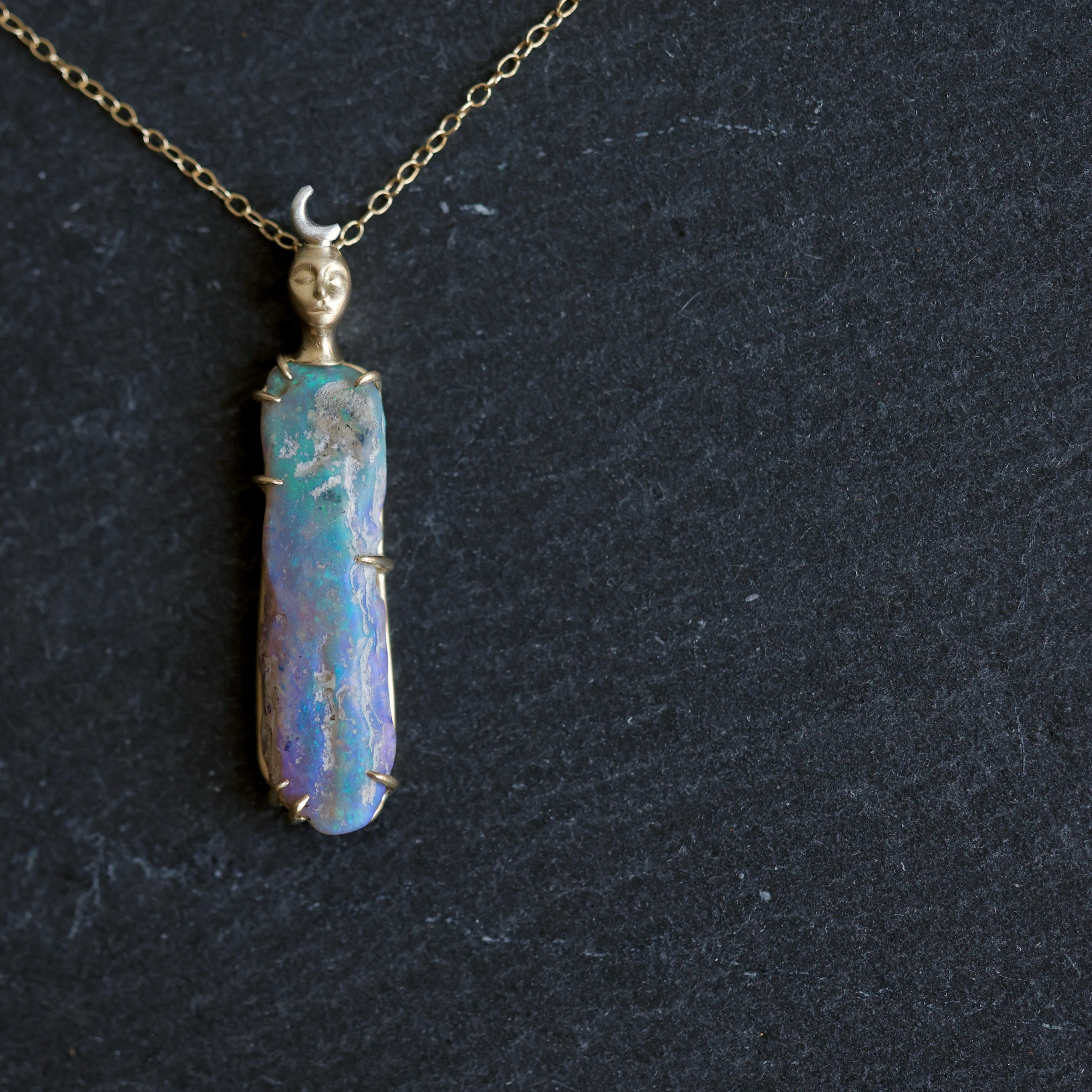 Necklace with a colorful opal and gold face with crescent moon on a slate surface