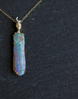 Necklace with a colorful opal and gold face with crescent moon on a slate surface