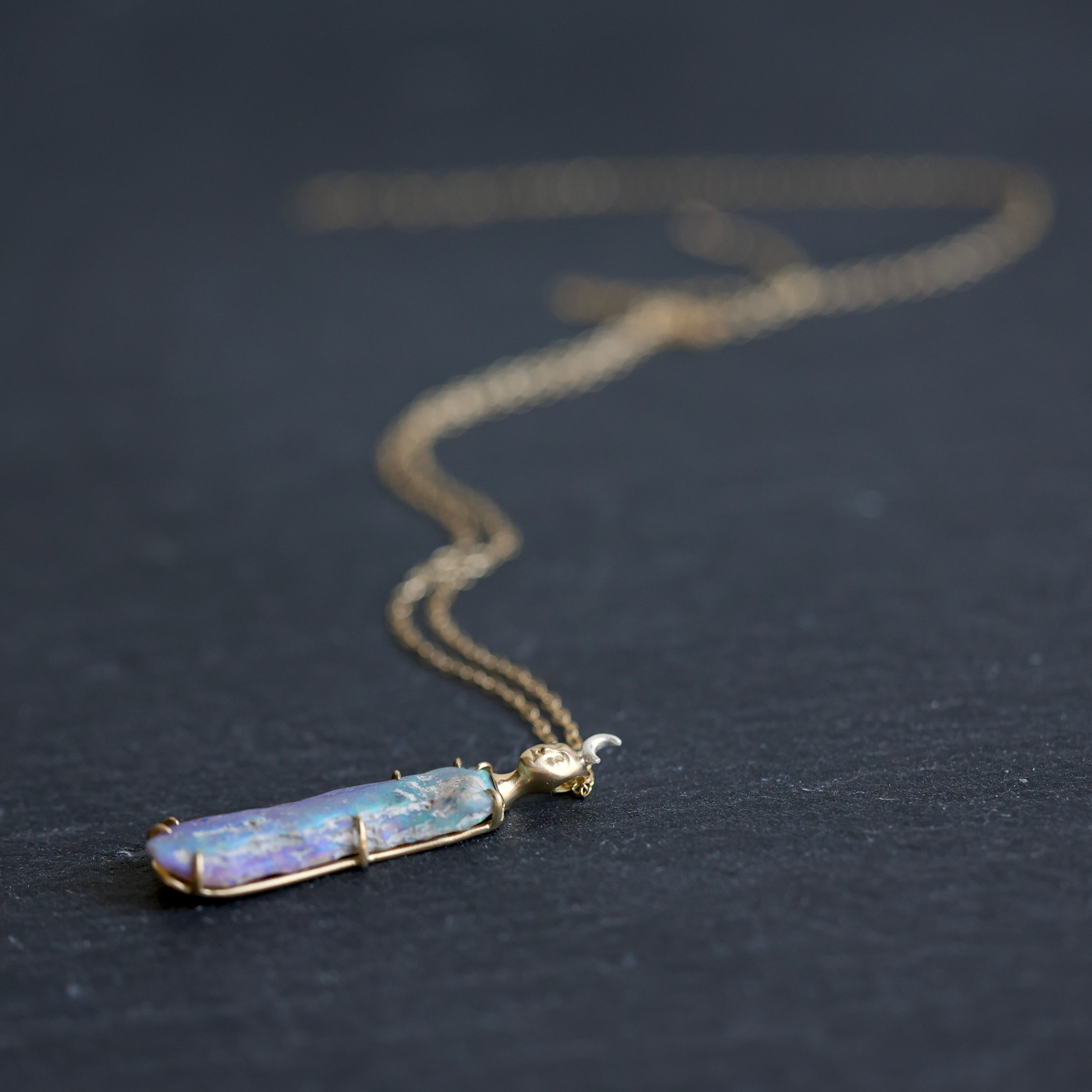 Necklace with a colorful opal and gold face with crescent moon on a slate surface
