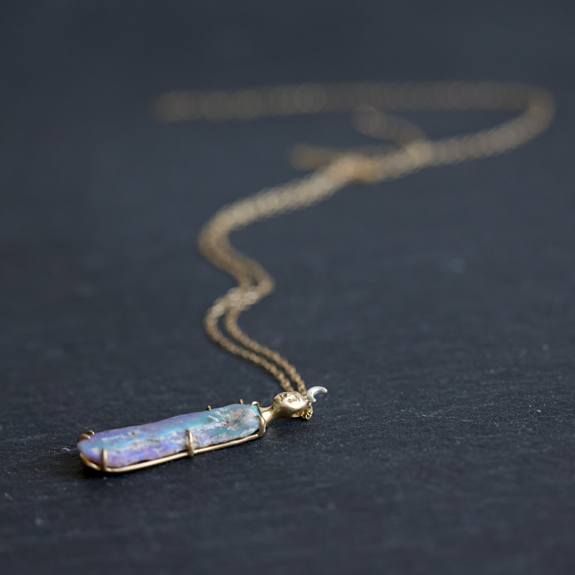 Necklace with a colorful opal and gold face with crescent moon on a slate surface