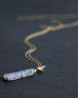 Necklace with a colorful opal and gold face with crescent moon on a slate surface