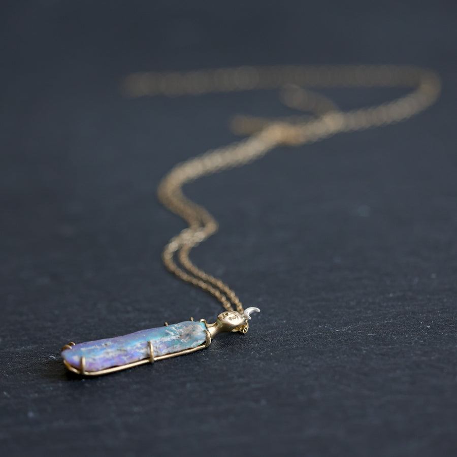Necklace with a colorful opal and gold face with crescent moon on a slate surface