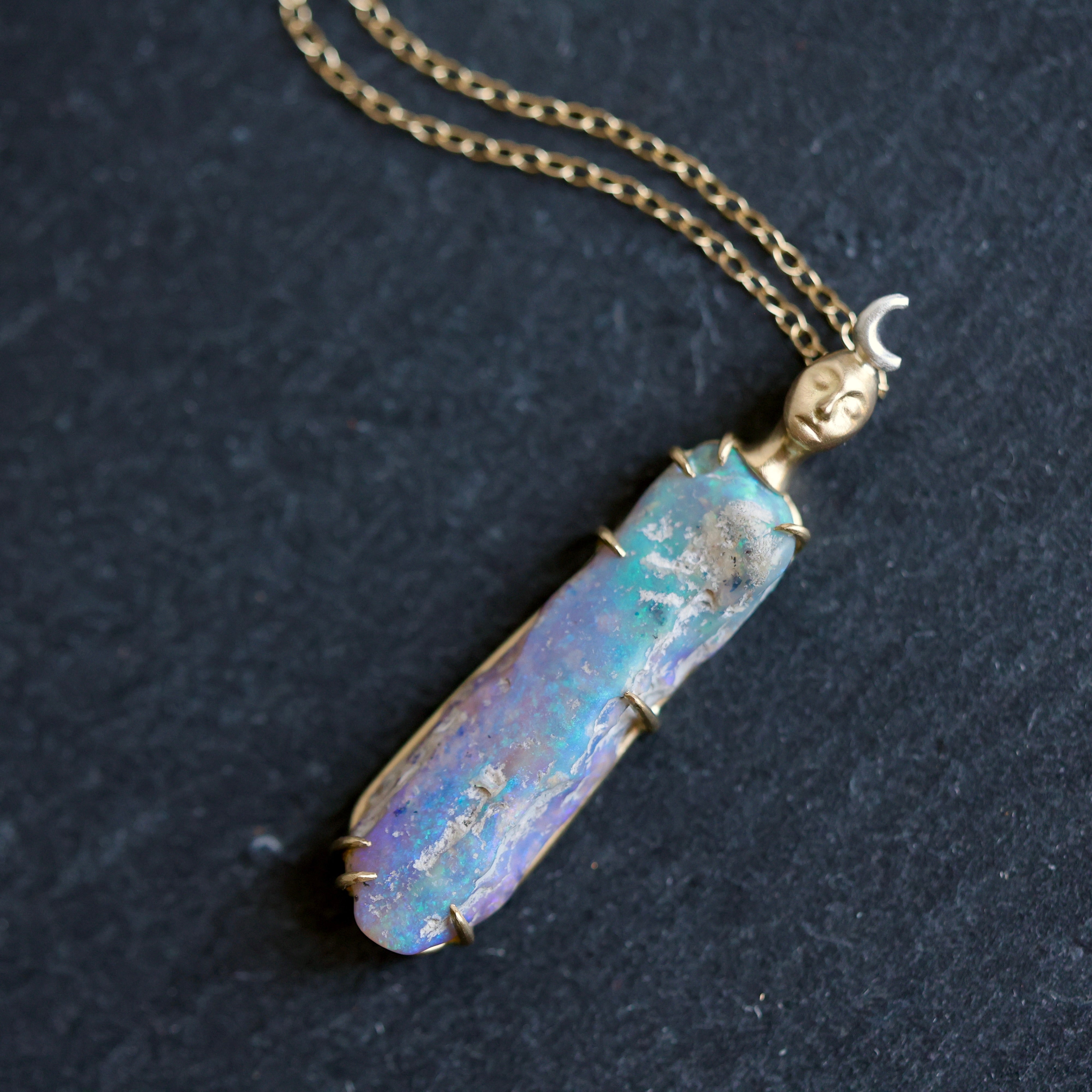 Necklace with a colorful opal and gold face with crescent moon on a slate surface