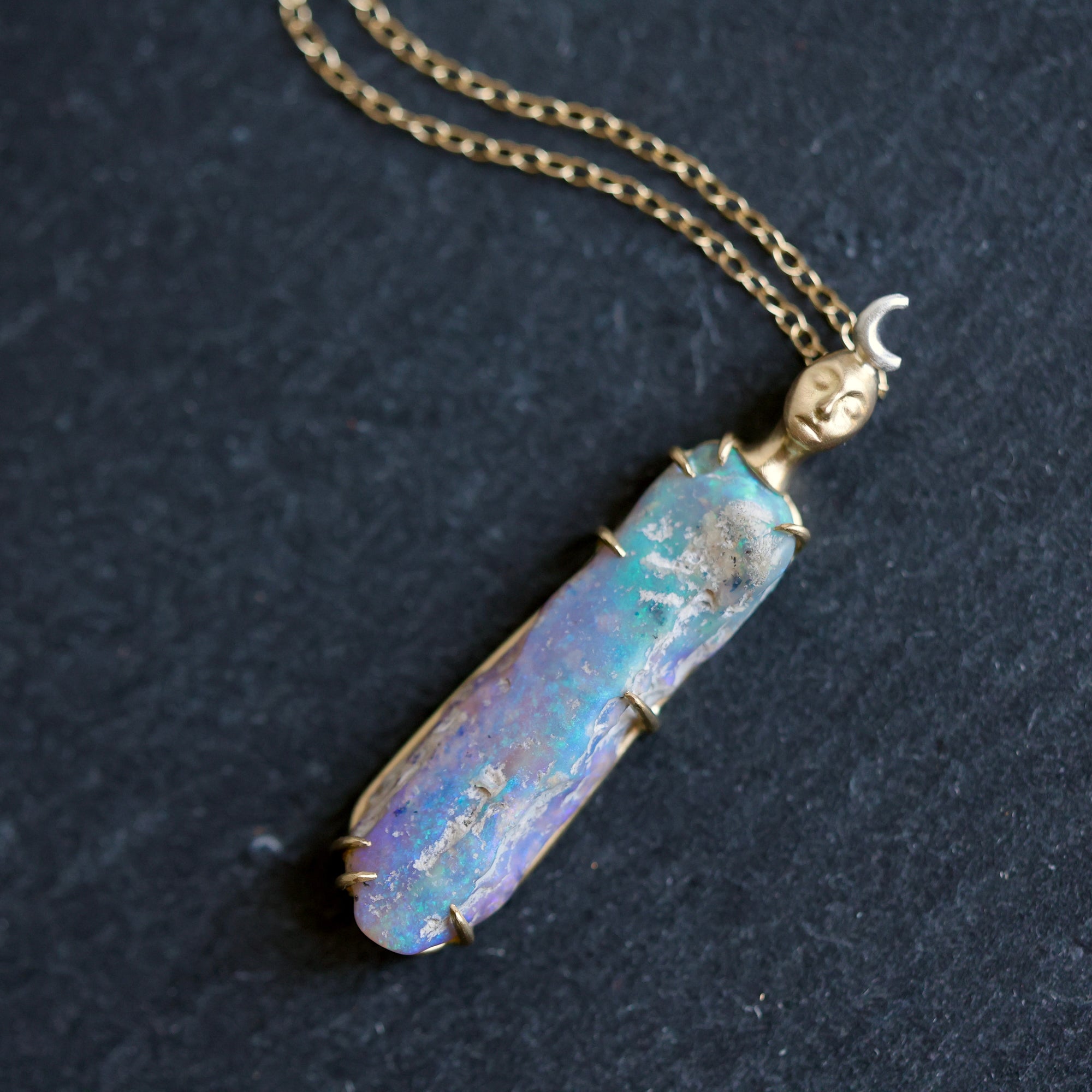 Necklace with a colorful opal and gold face with crescent moon on a slate surface