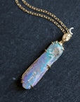 Necklace with a colorful opal and gold face with crescent moon on a slate surface