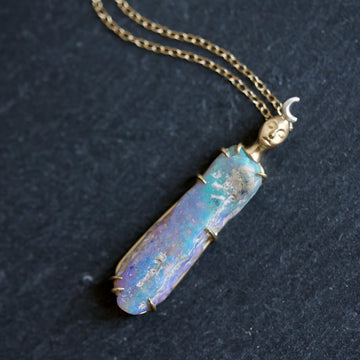 Necklace with a colorful opal and gold face with crescent moon on a slate surface