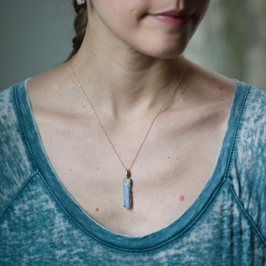 Person wearing a necklace with a blue pendant, blurred background