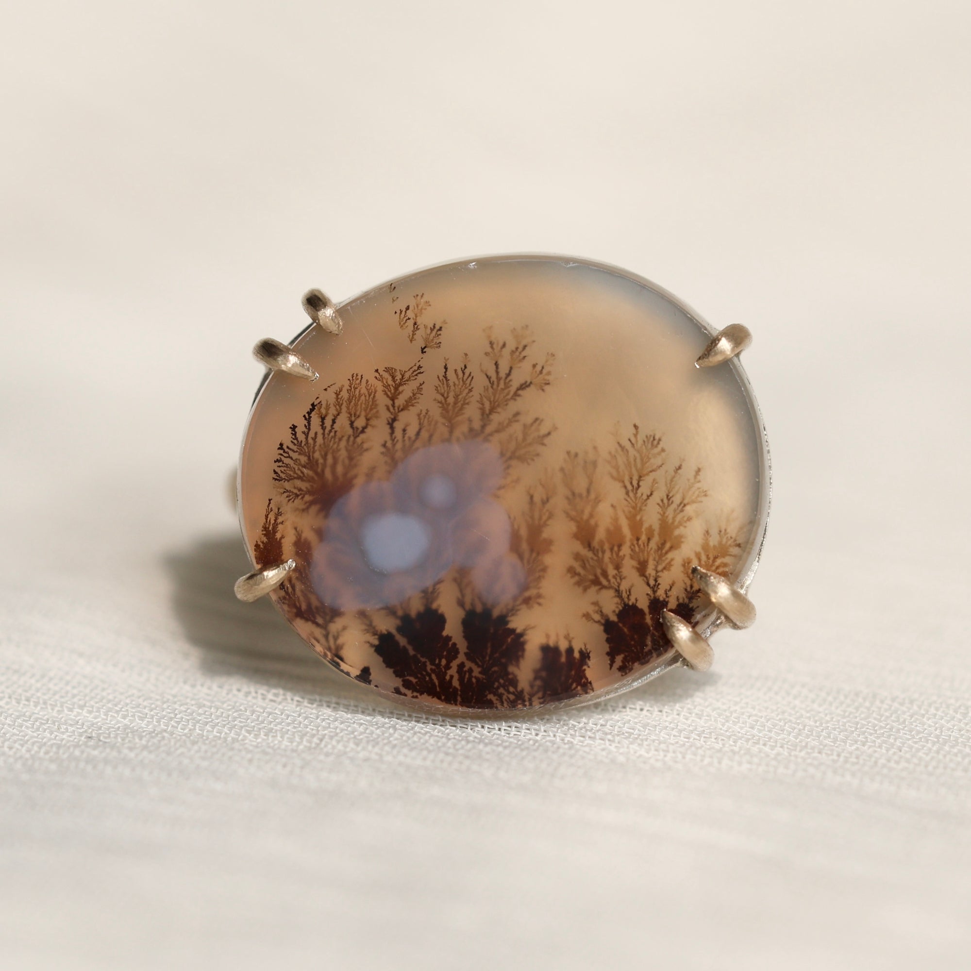 Oval agate stone with tree pattern on a white fabric background