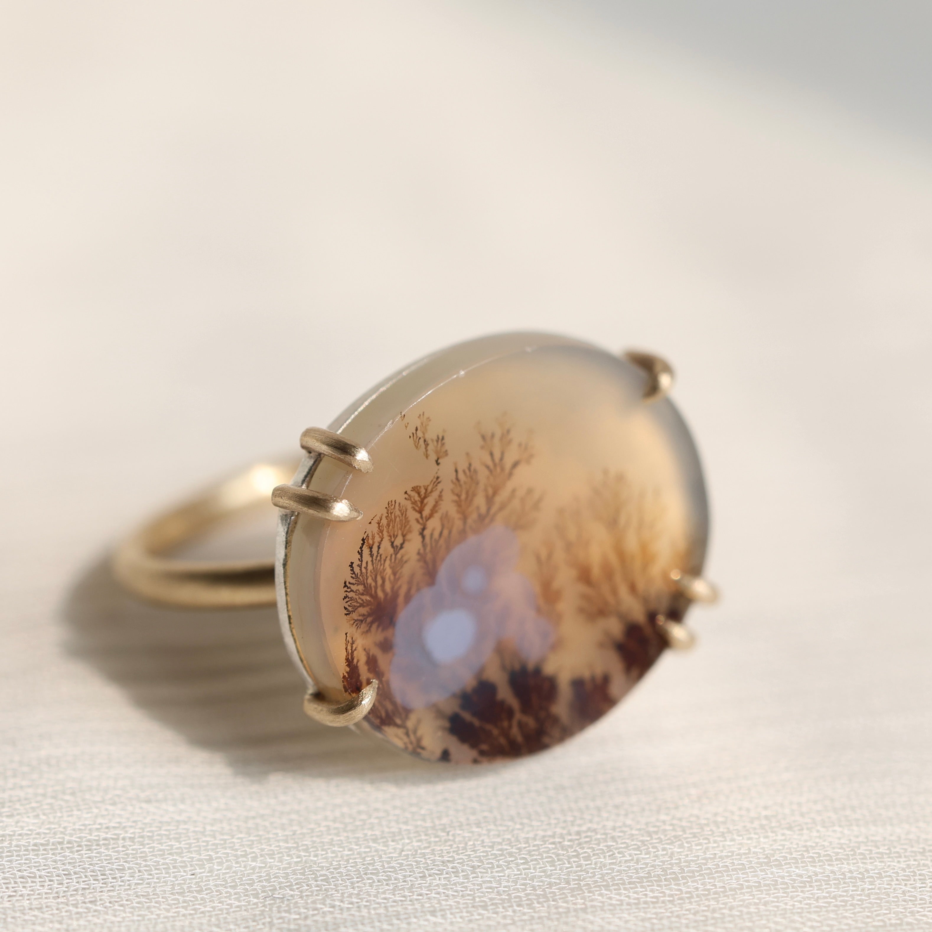 Oval agate stone with tree pattern on a white fabric background