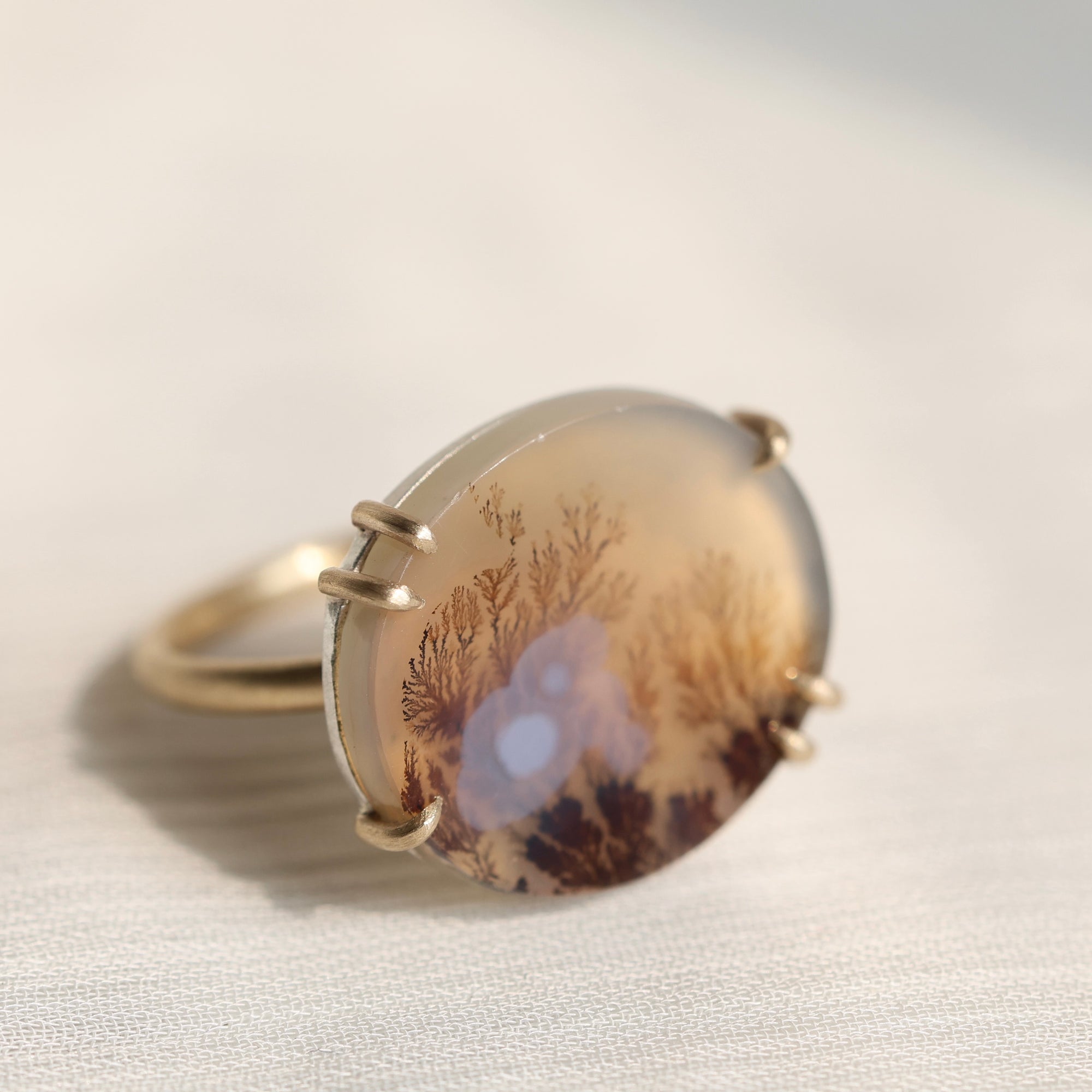 Oval agate stone with tree pattern on a white fabric background