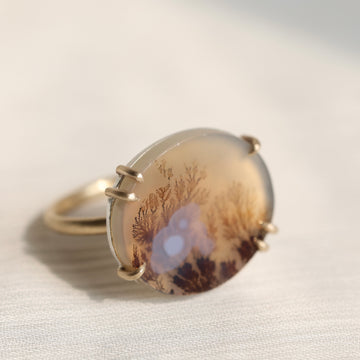 Oval agate stone with tree pattern on a white fabric background