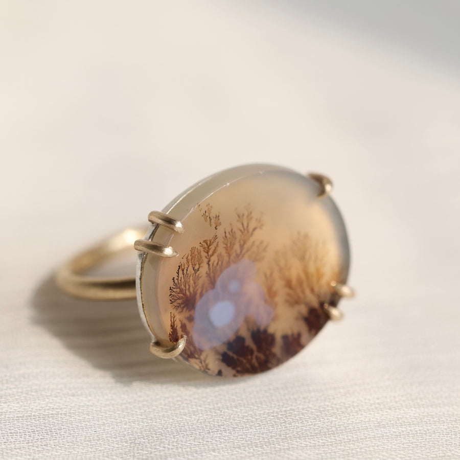 Oval agate stone with tree pattern on a white fabric background