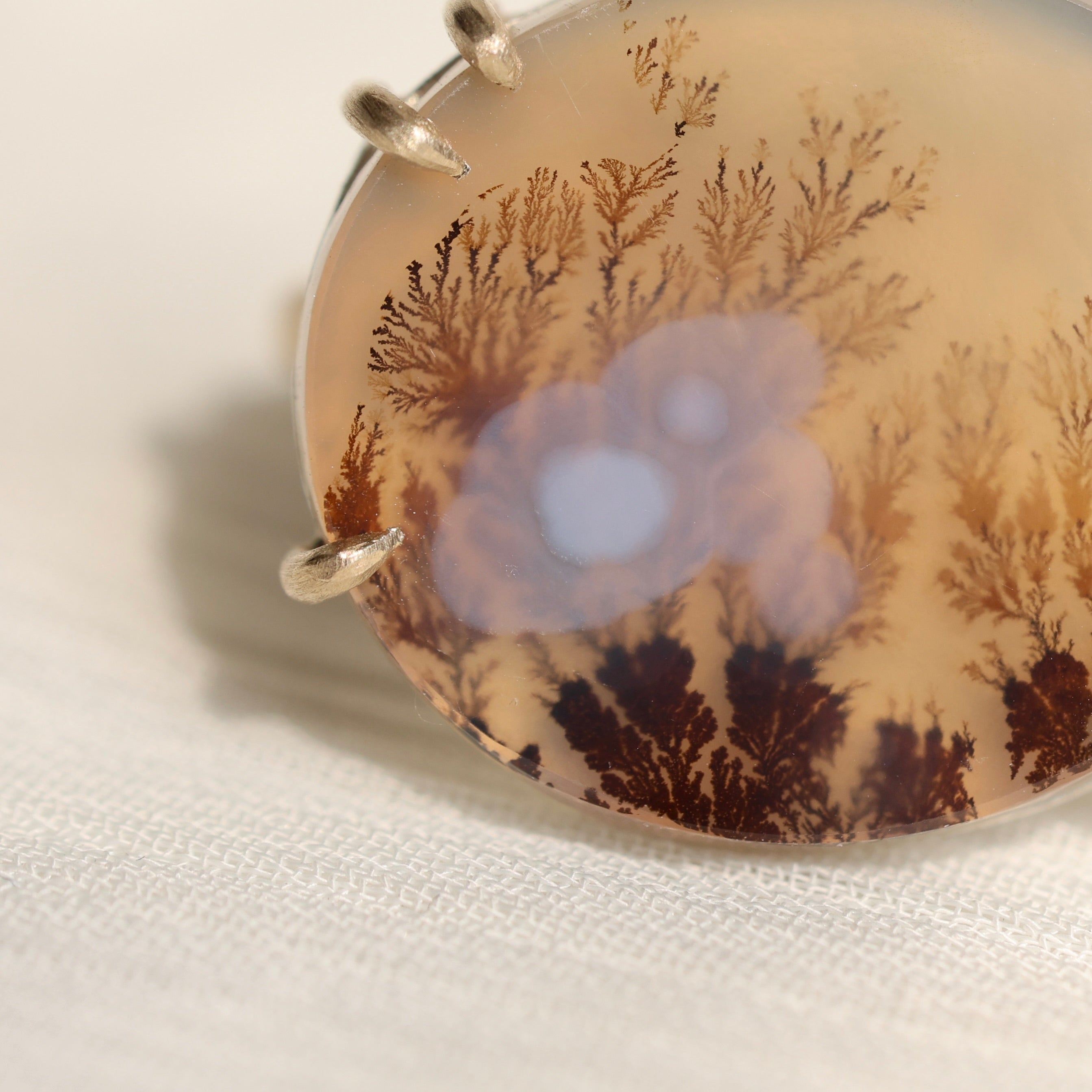 Oval agate stone with tree pattern on a white fabric background