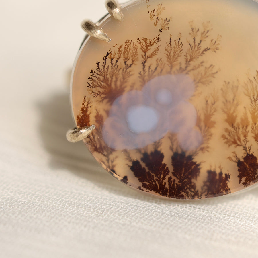 Oval agate stone with tree pattern on a white fabric background
