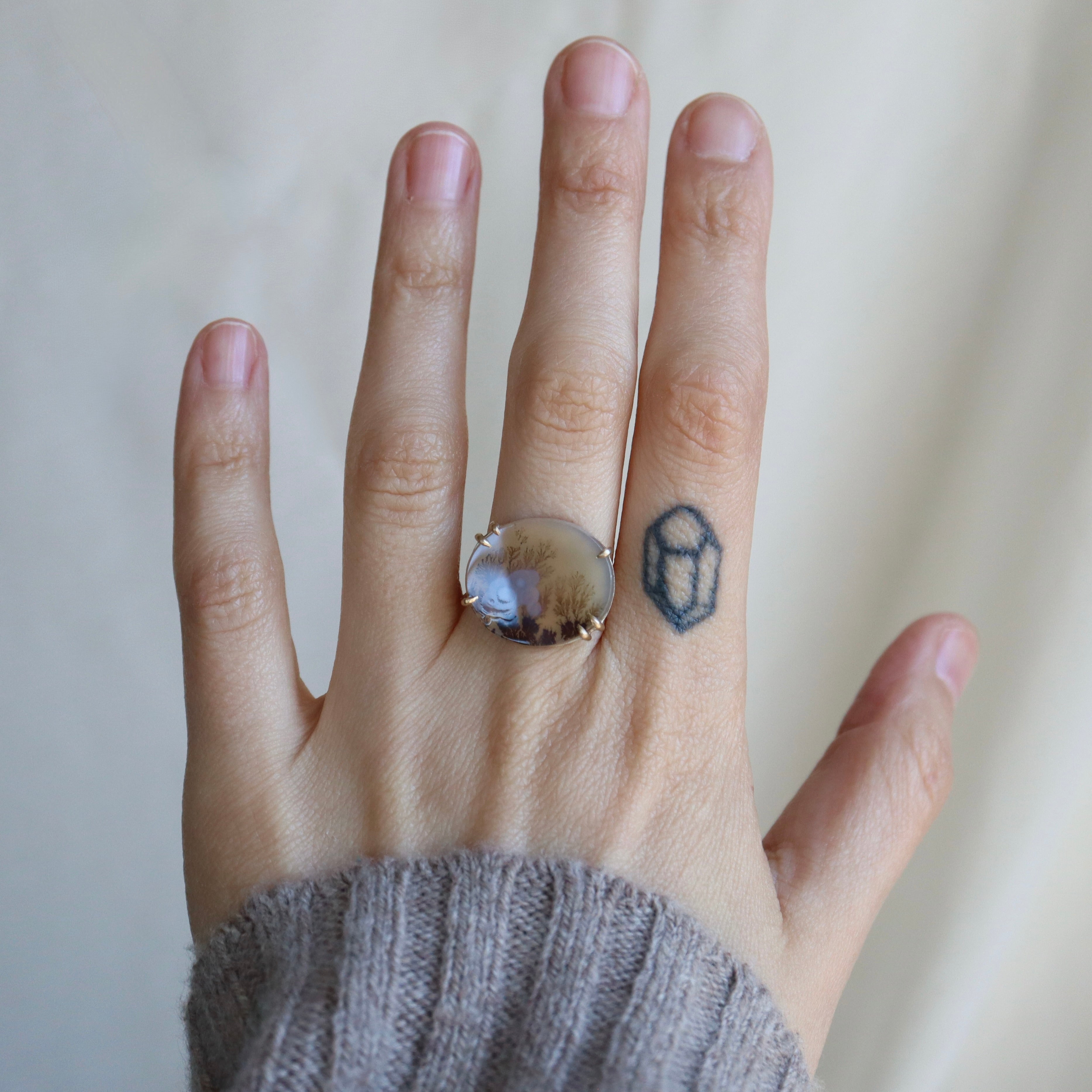 hand wearing large beige, brown and gold ring against a pale background