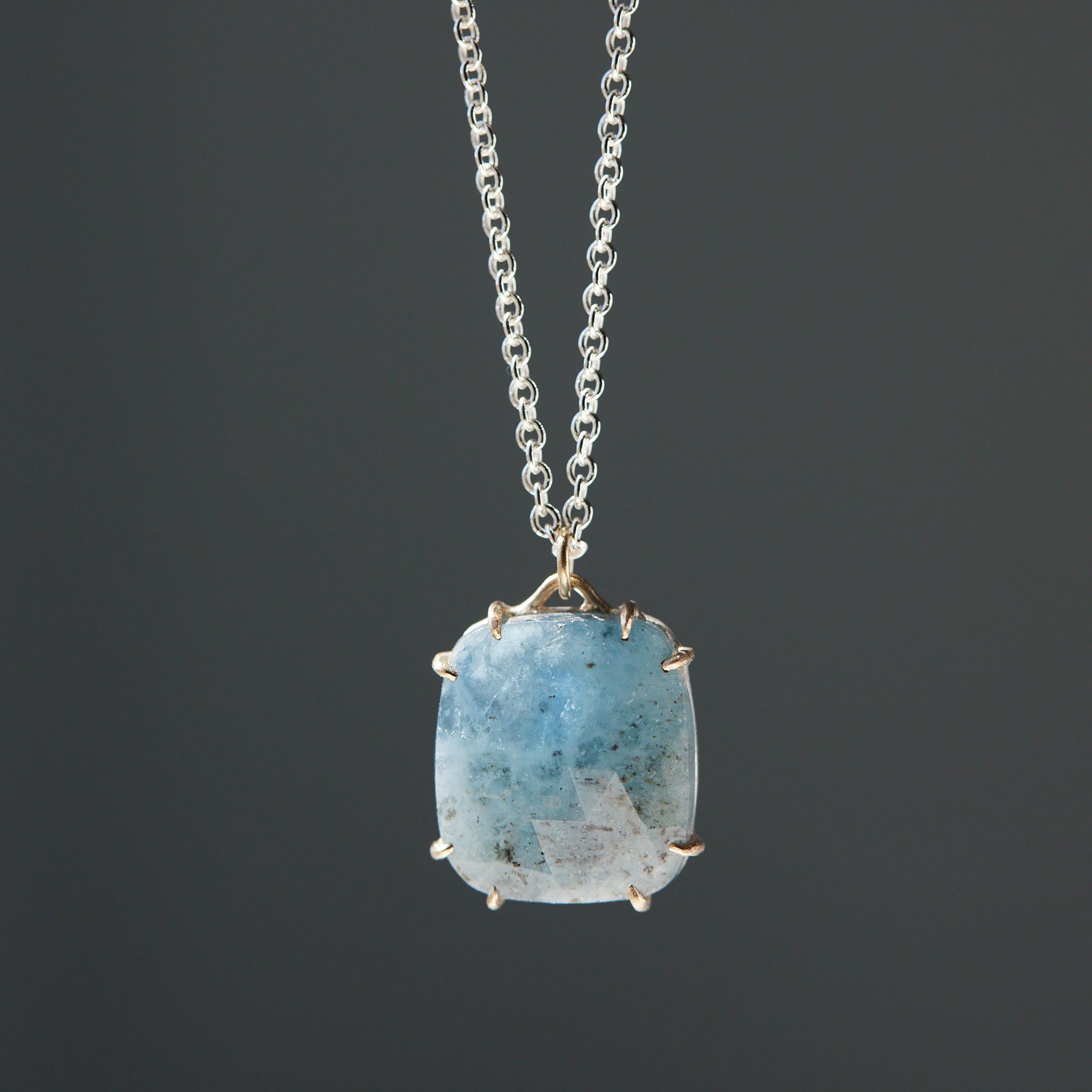 rounded square aquamarine pendant with gold prongs and a silver chain.