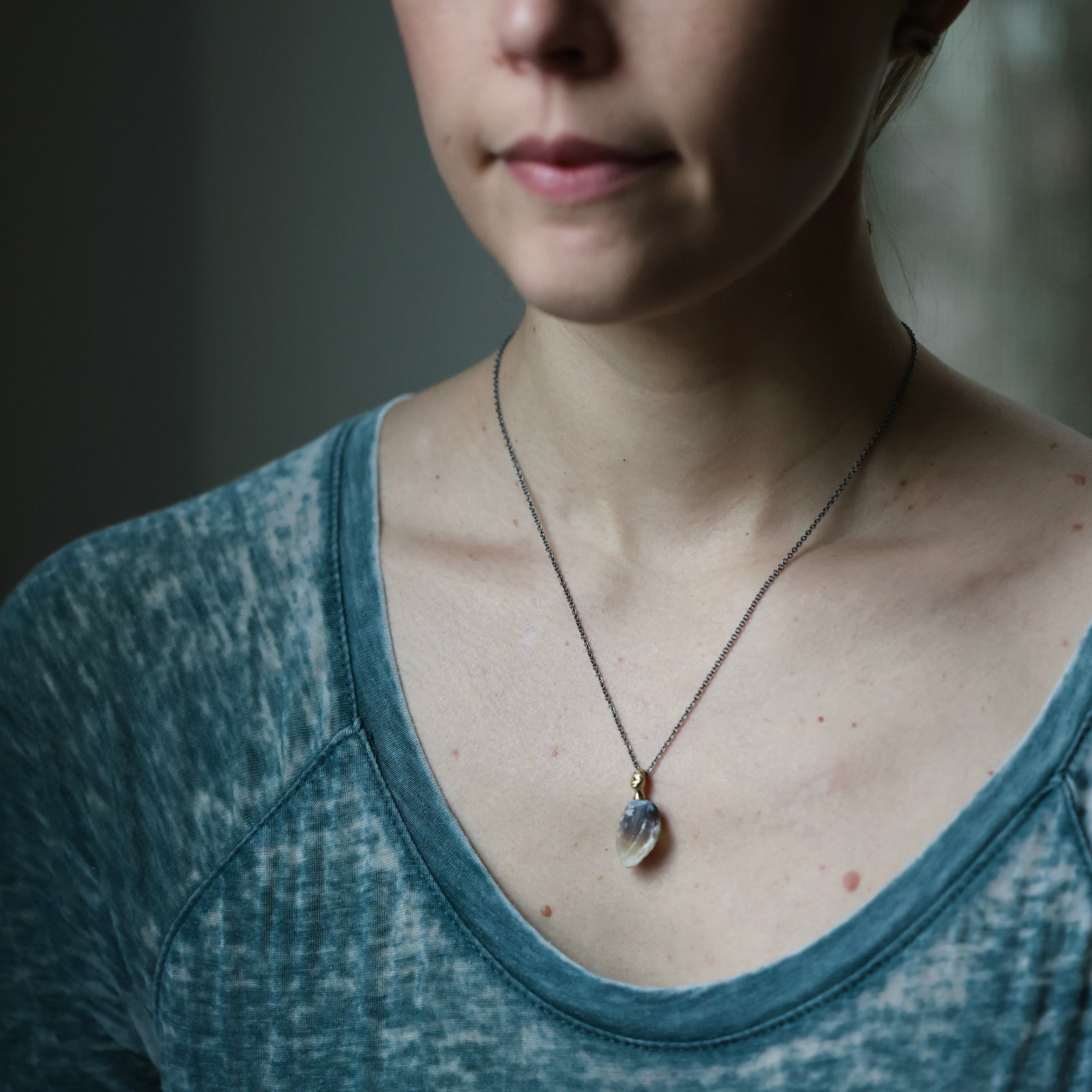 Person wearing a necklace with a pendant against a neutral background