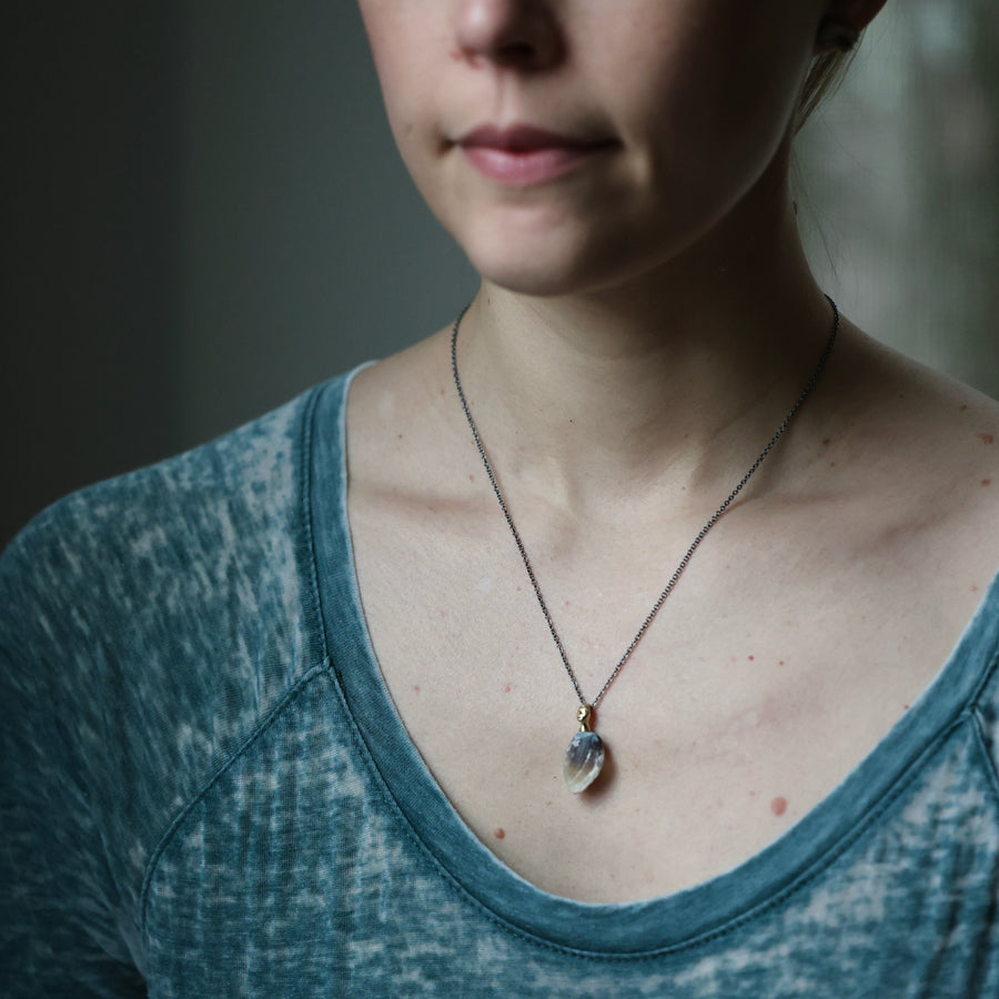 Person wearing a necklace with a pendant against a neutral background