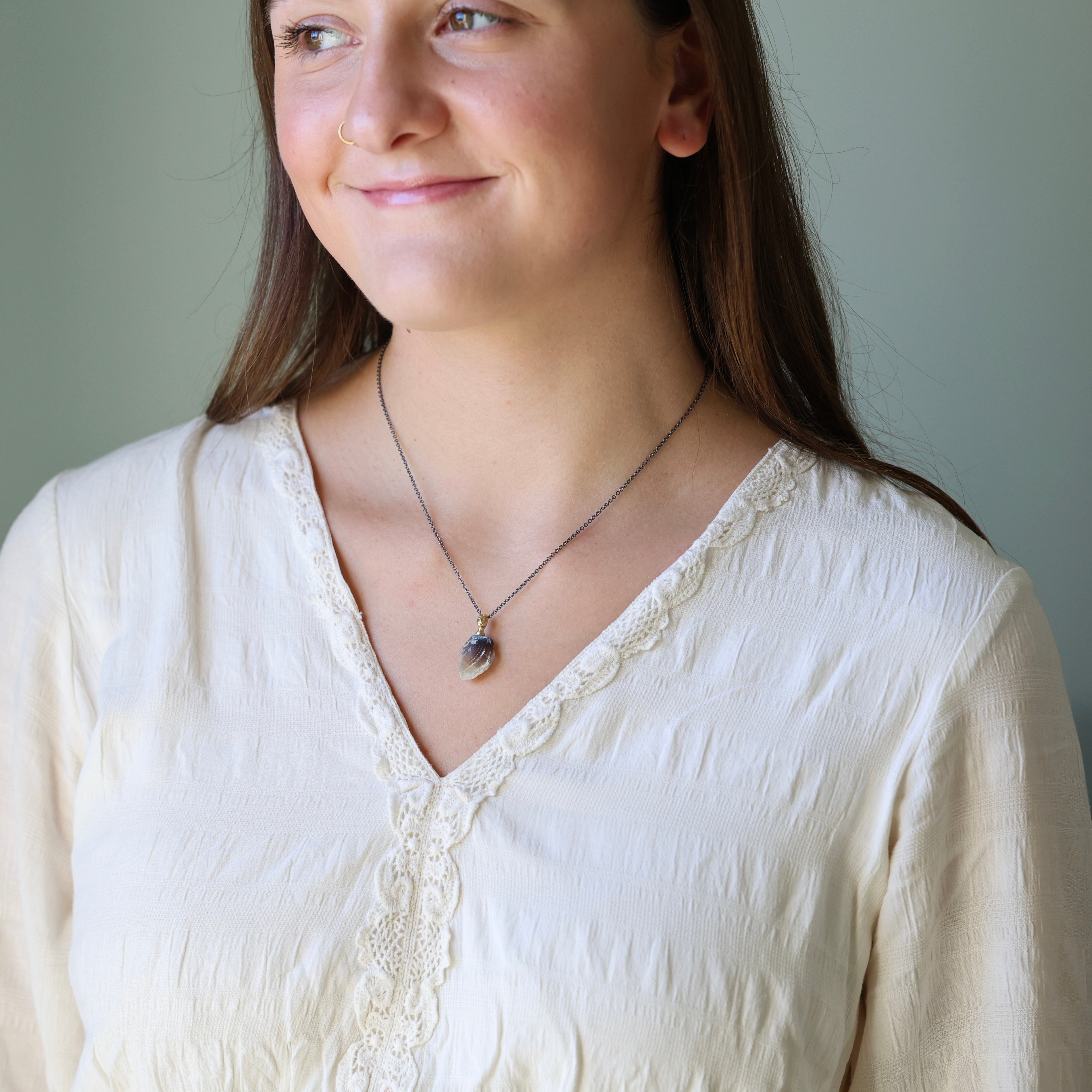 Woman wearing a white blouse and necklace against a plain background