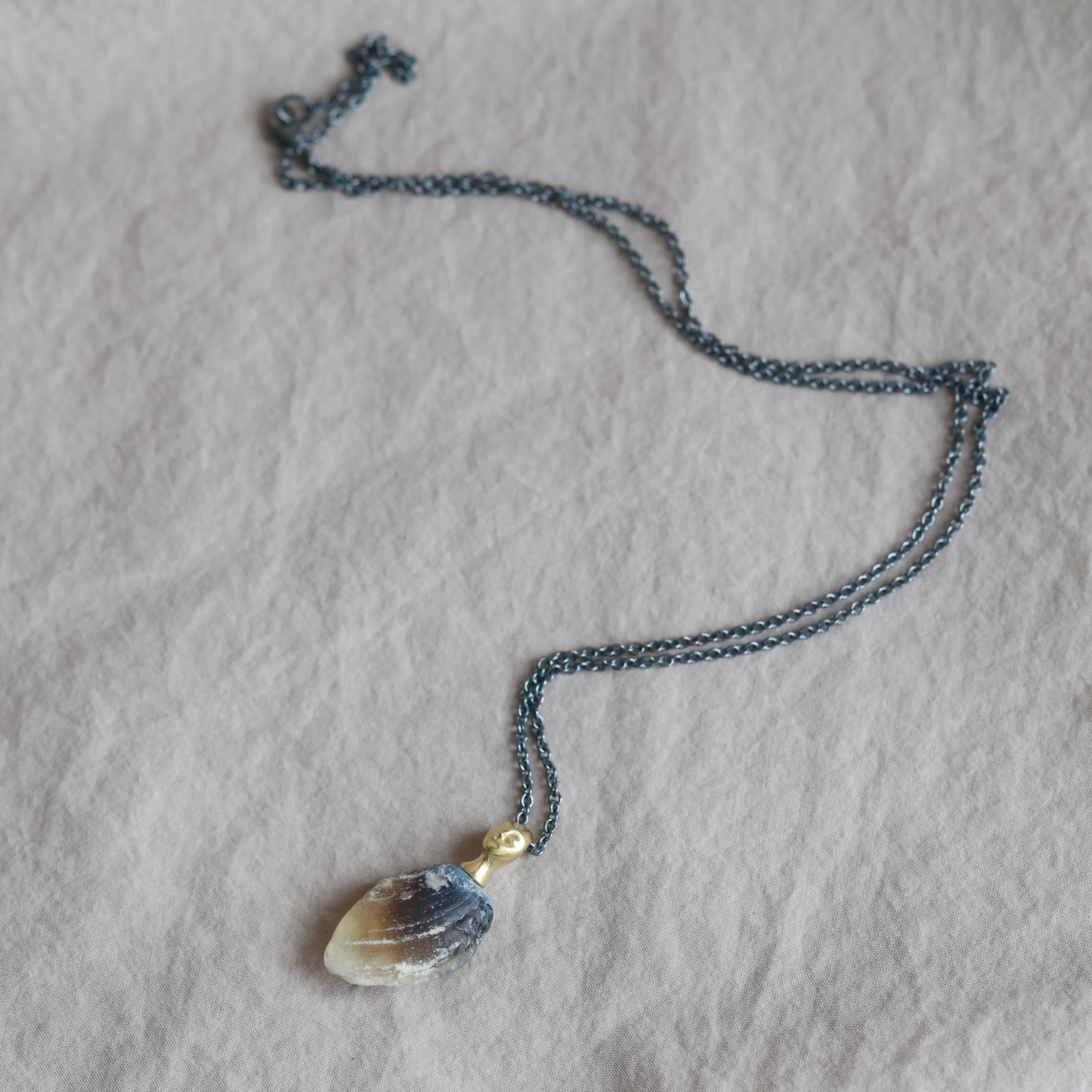 Necklace with a clambshell fossil pendant on a textured fabric background