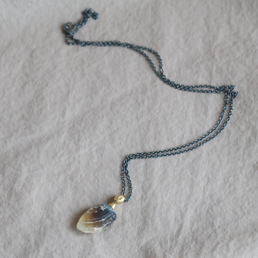 Necklace with a clambshell fossil pendant on a textured fabric background