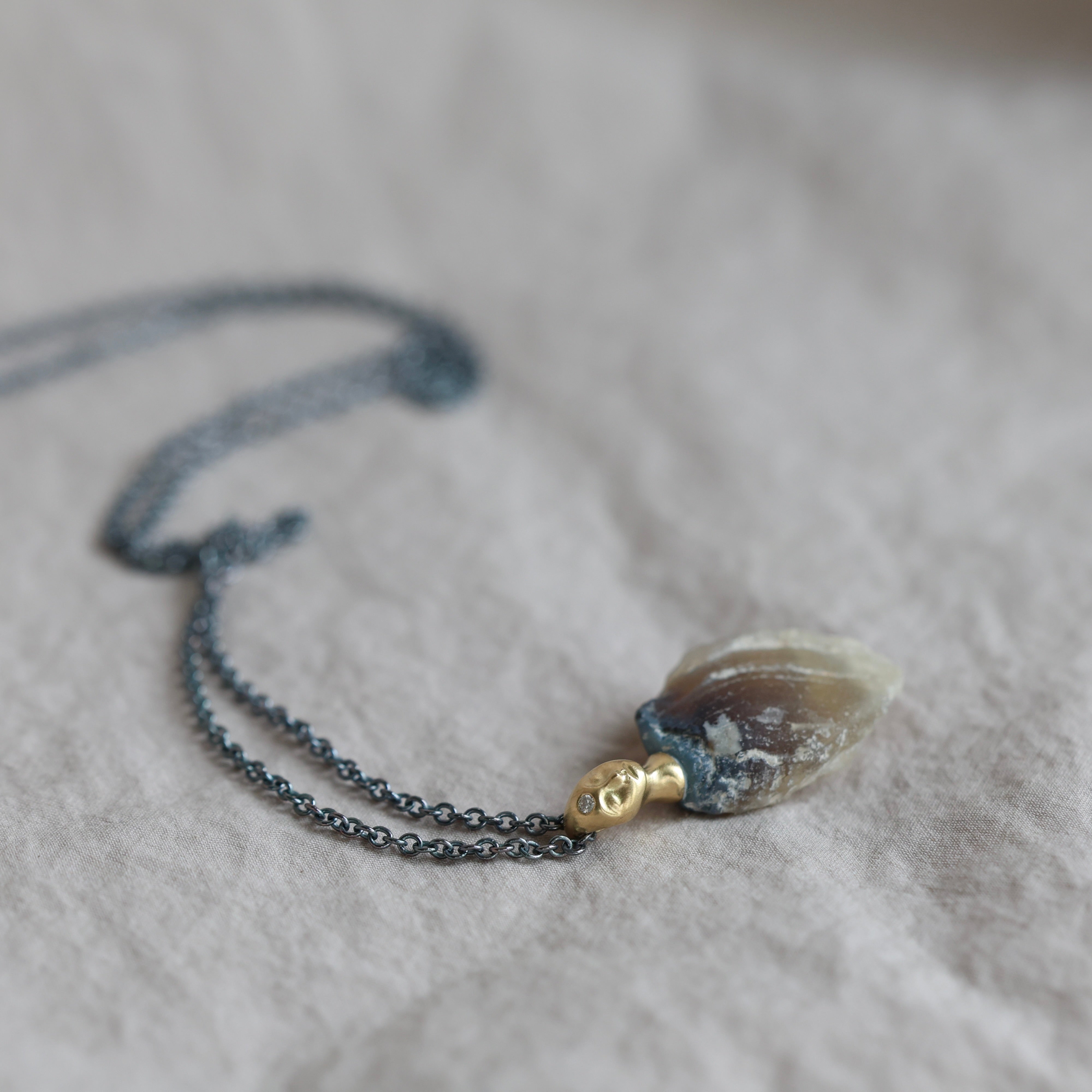 Necklace with a clambshell fossil pendant on a textured fabric background