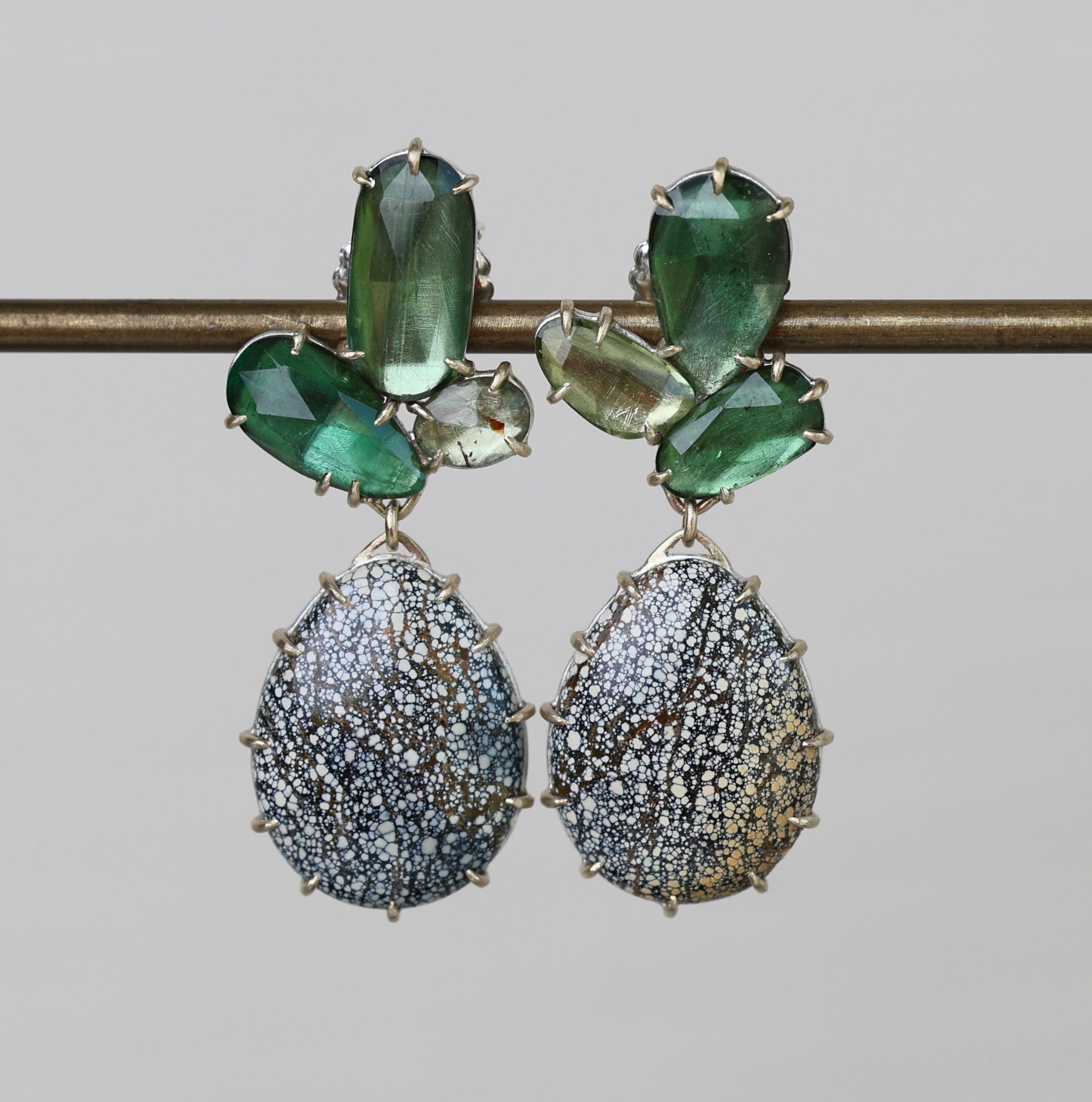 Pair of earrings with green gemstones and textured silver drops on a gray background